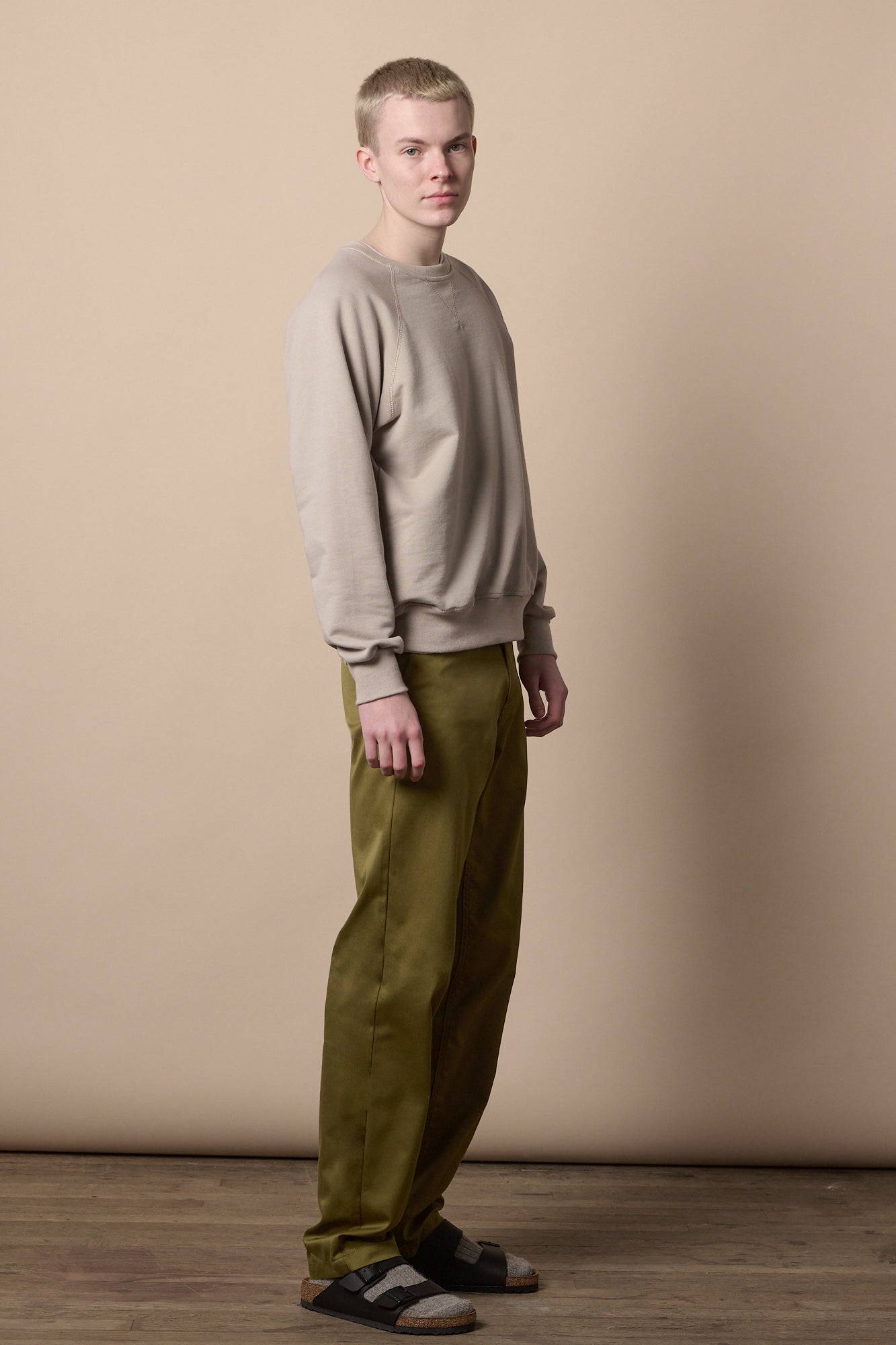 Full body image of white male wearing relaxed chino in moss paired with sweatshirt in stone