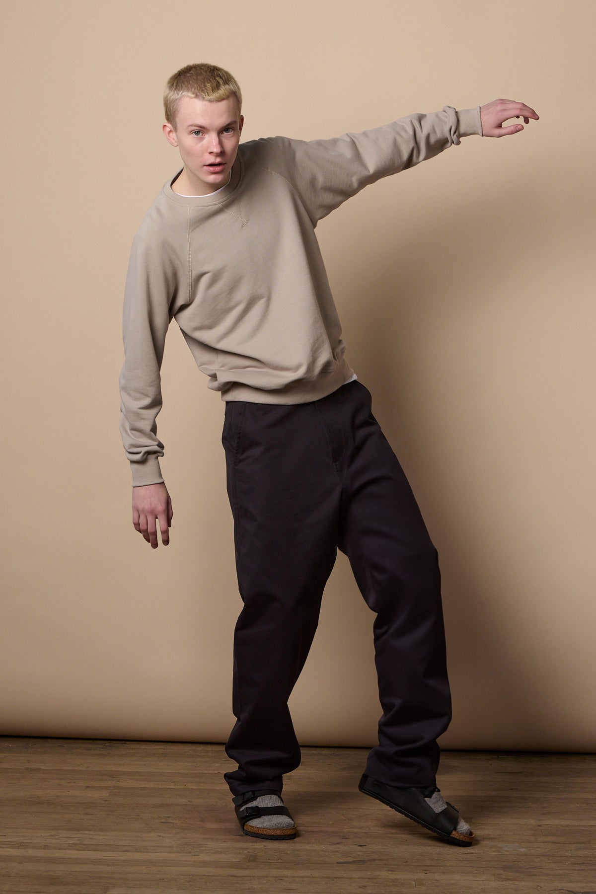 
            Full body image of white male with short blonde hair balancing onto one leg with arm up, wearing men&#39;s relaxed chino in navy  