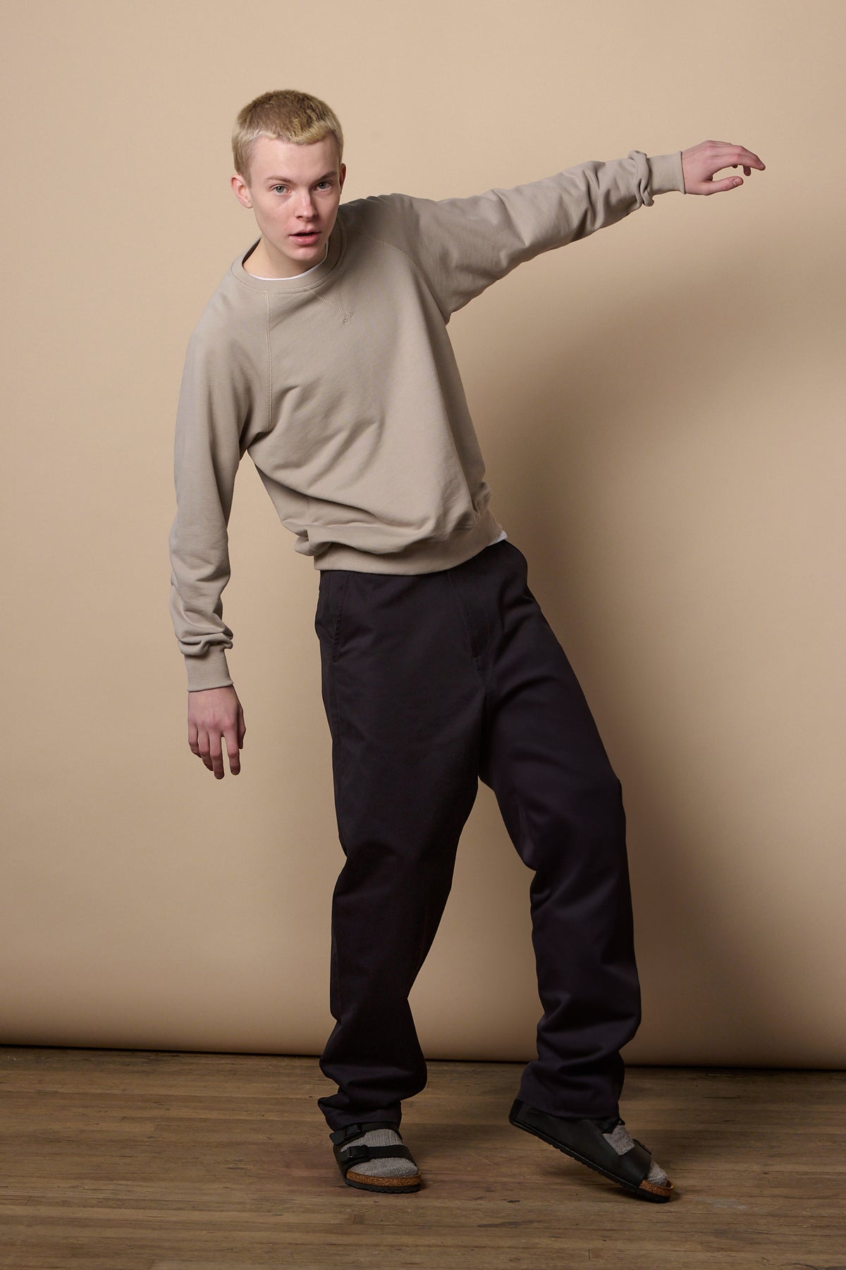 Full body image of white male with short blonde hair balancing onto one leg with arm up, wearing men's relaxed chino in navy