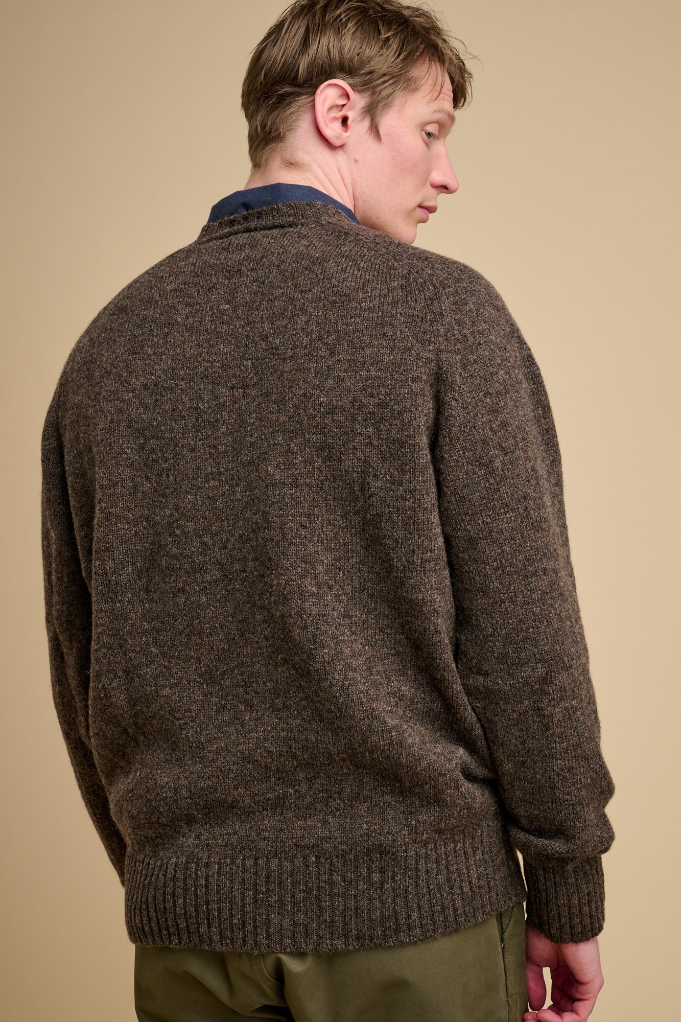 The back of man wearing a brown sweater against a beige background.