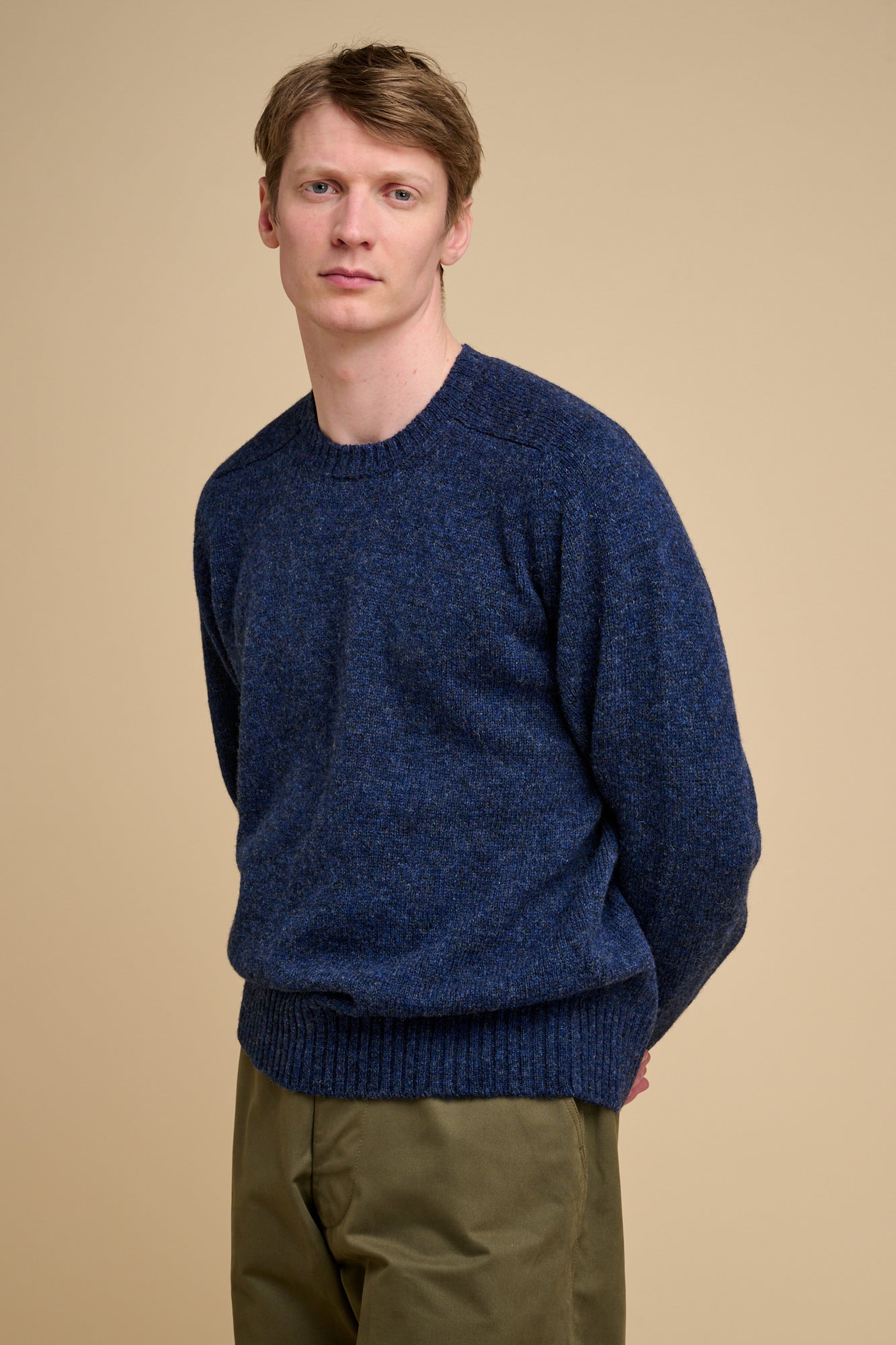 Man wearing a blue Knit jumper against a beige background.