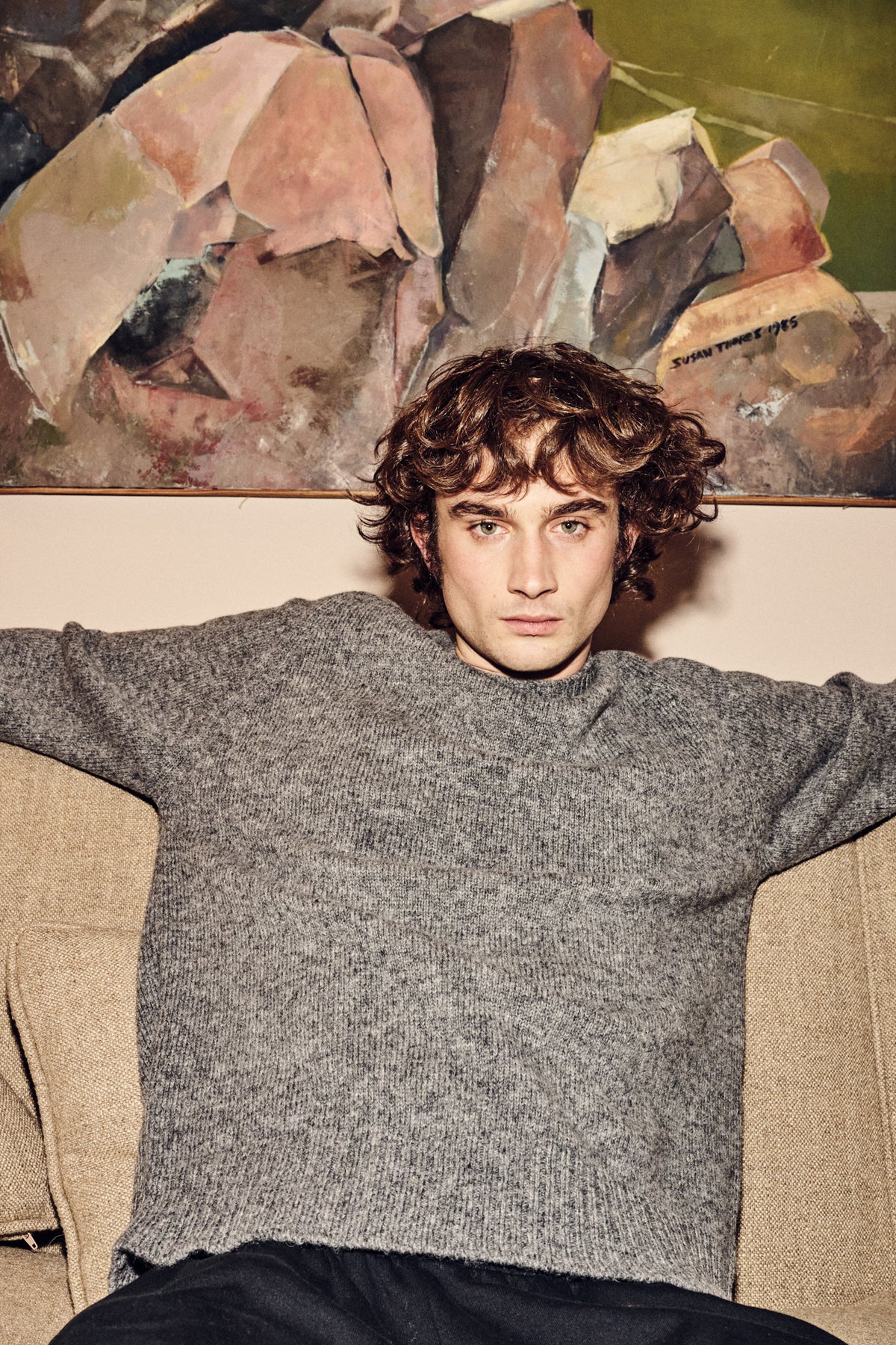 Man wearing a grey sweater sitting on a couch with abstract painting in the background