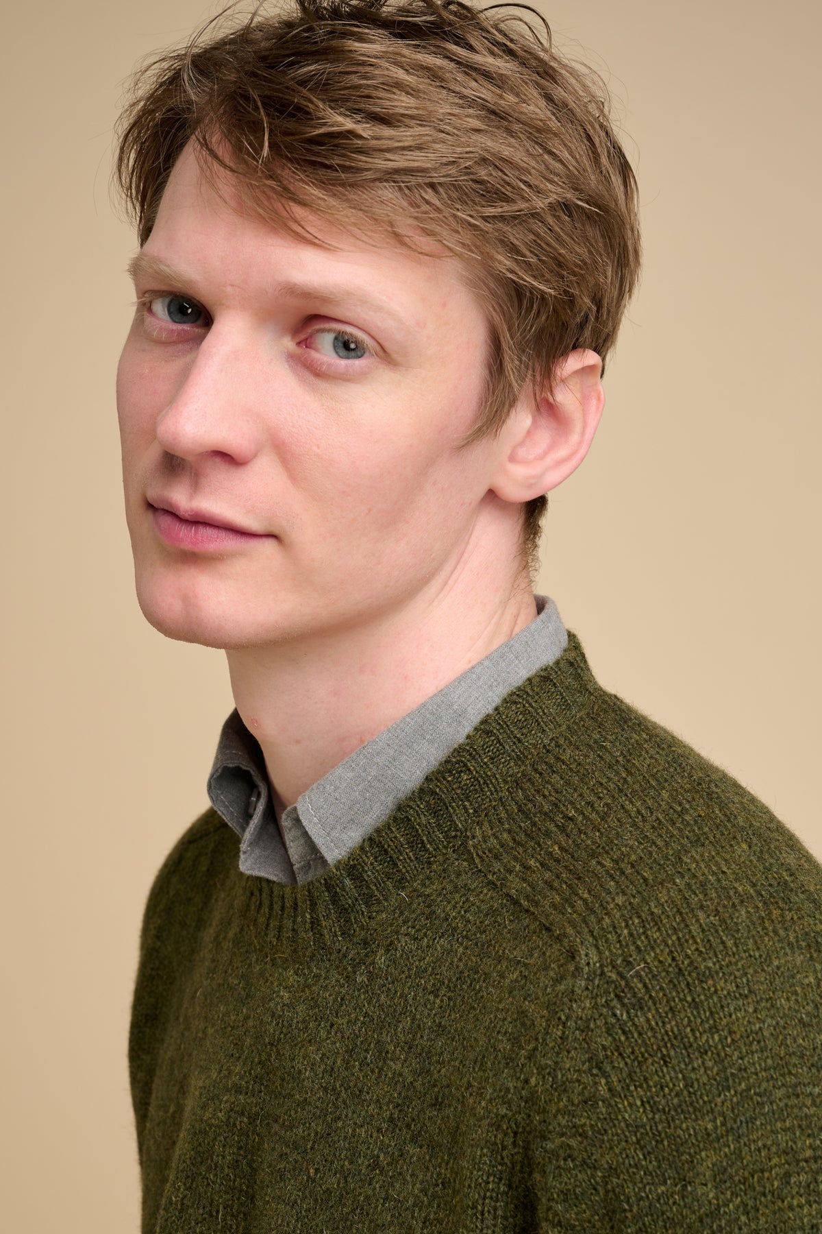 Man wearing a green sweater over a collared shirt on a beige background