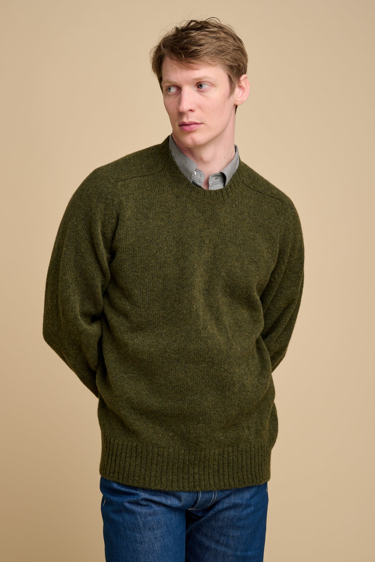Man wearing a green sweater over a collared shirt on a beige background.