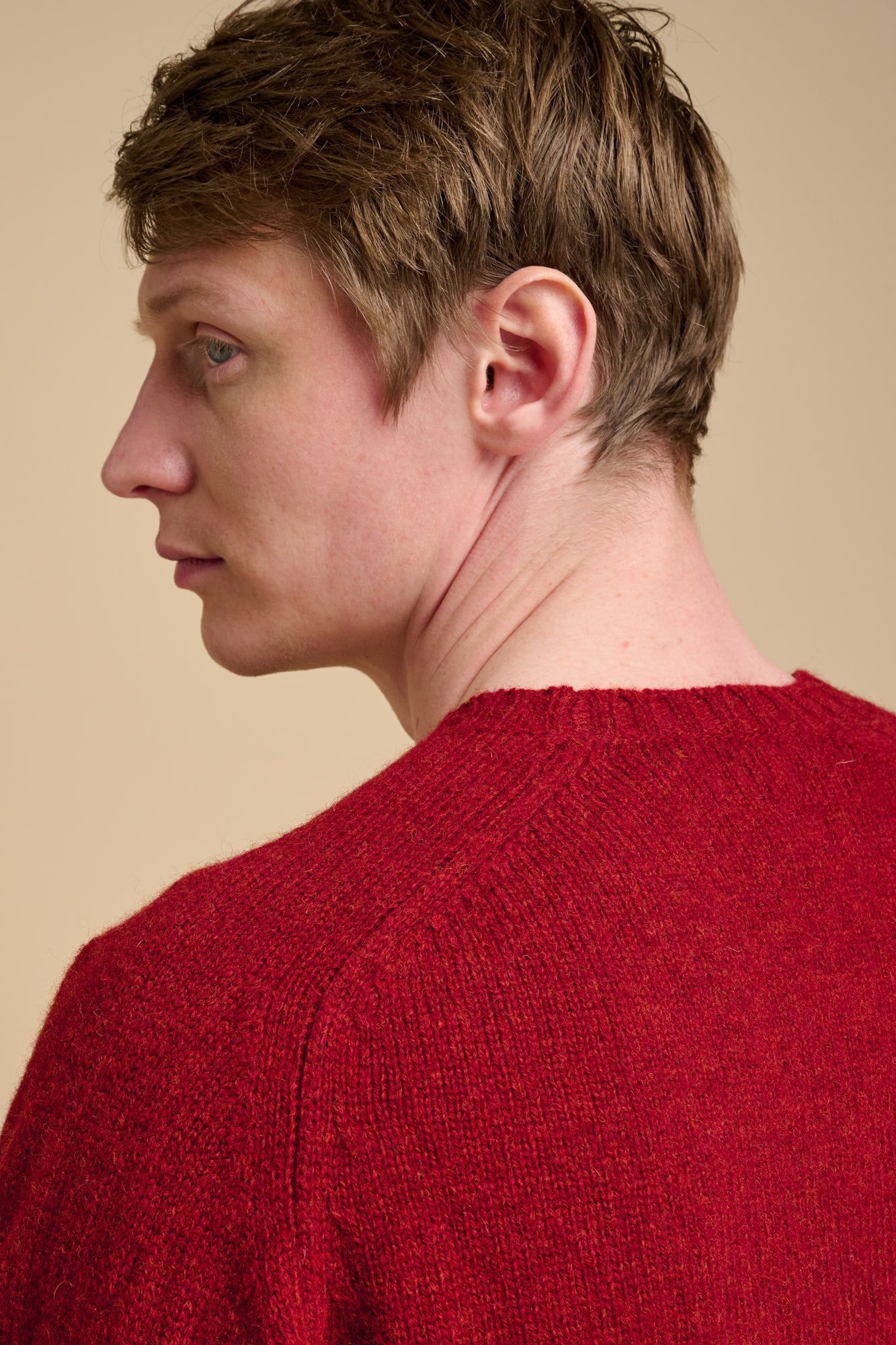 Person wearing a red sweater against a beige background