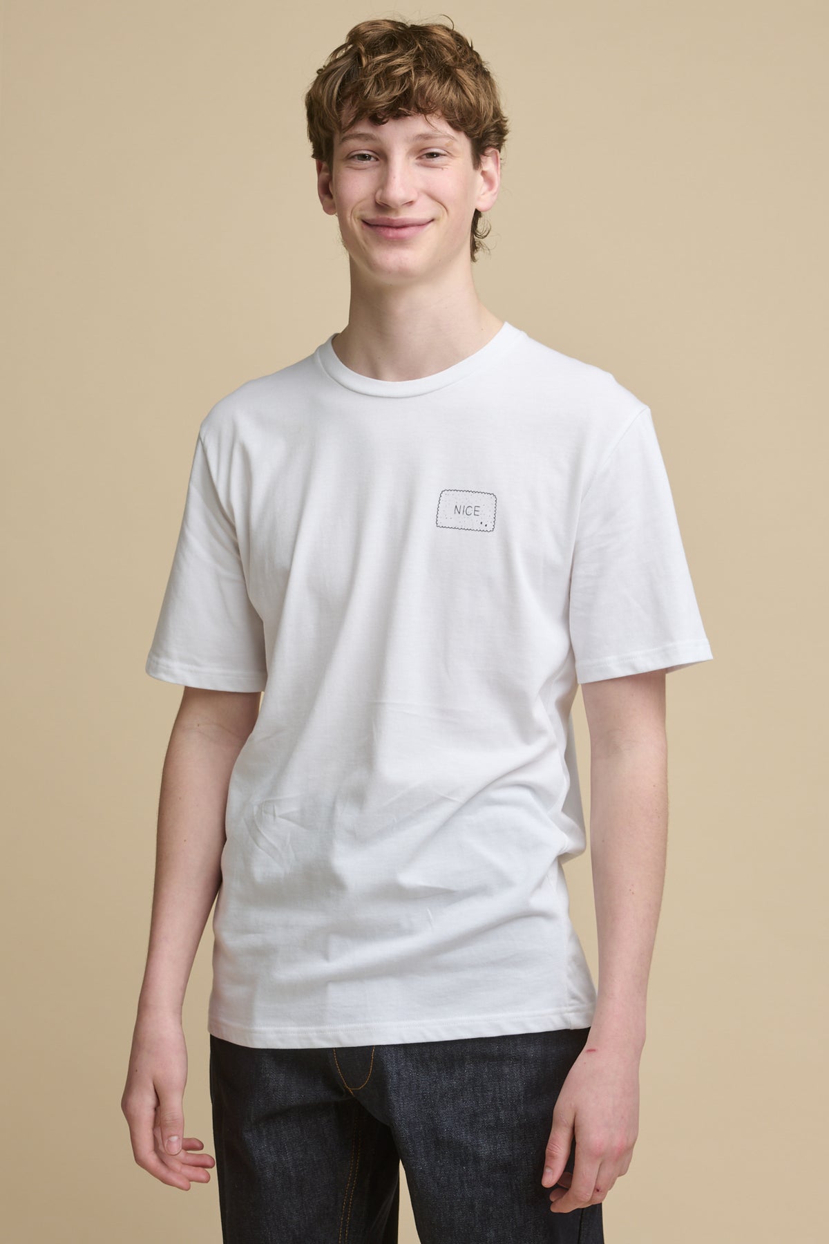 
            Thigh up image of the front of smiley male wearing short sleeve white graphic t shirt with &#39;Nice&#39; biscuit print on the chest