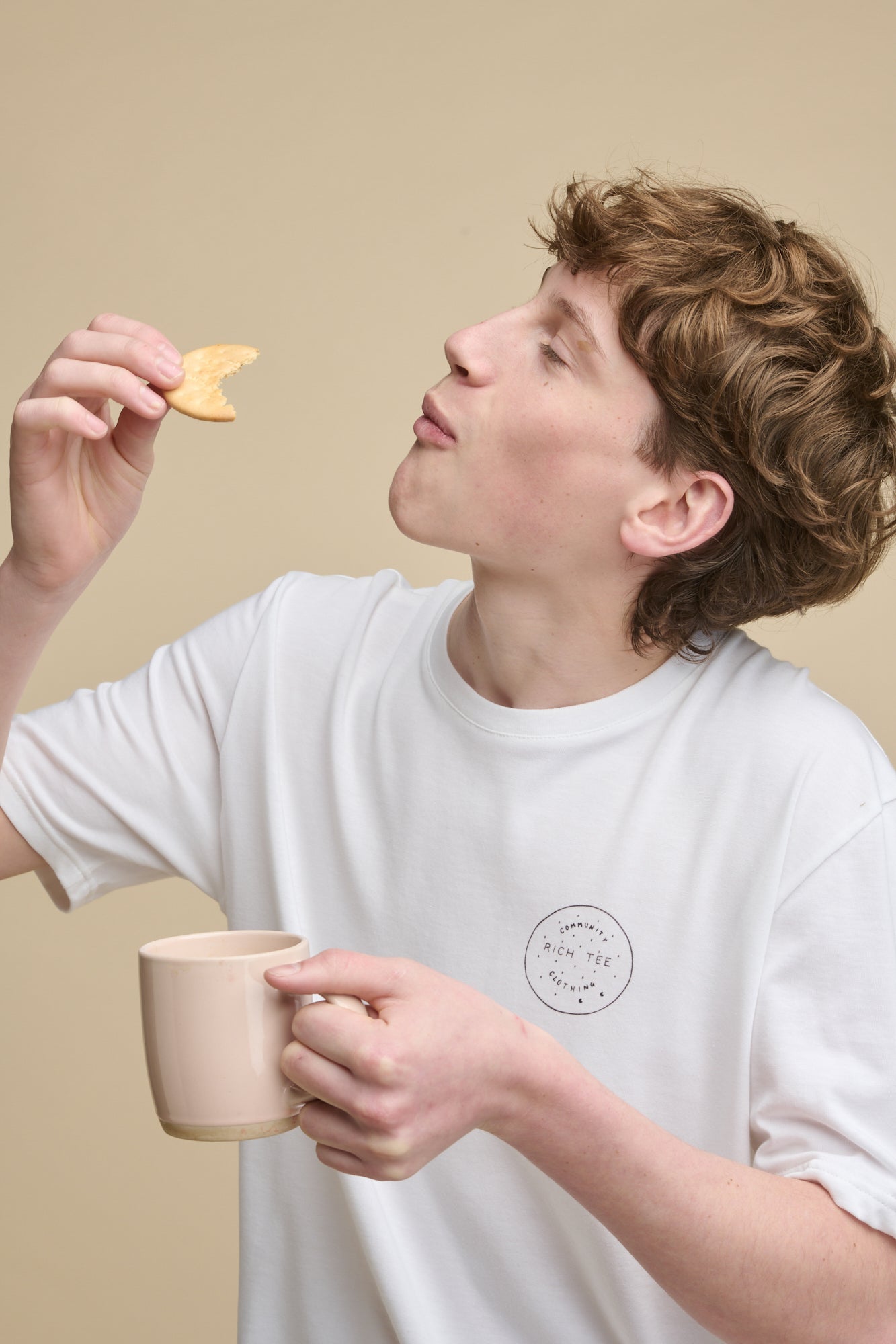 Portrait of male holding a rich tea biscuit dipped into a mug of tea wearing short sleeve graphic t shirt with rich tee biscuit print, holding a rich tea biscuit.