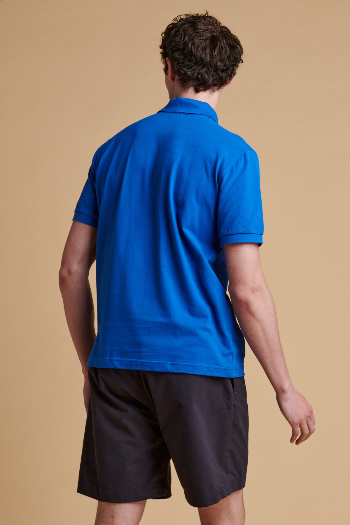 Thigh up of the back of male wearing short sleeve polo shirt in cobalt.