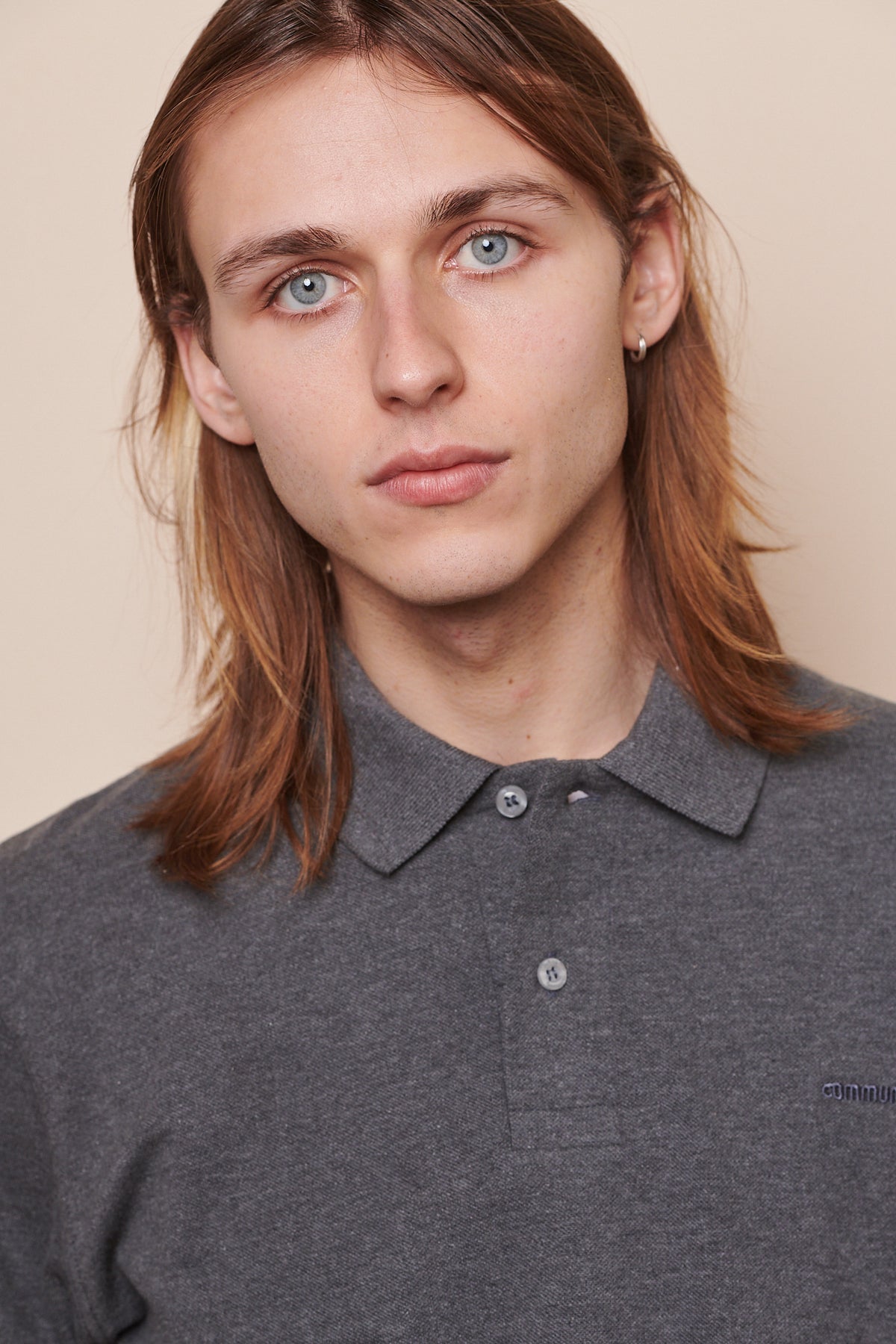 
            Portrait of male wearing polo shirt in grey marl with top button undone. &#39;Community&#39; embroidered in matching grey thread on chest