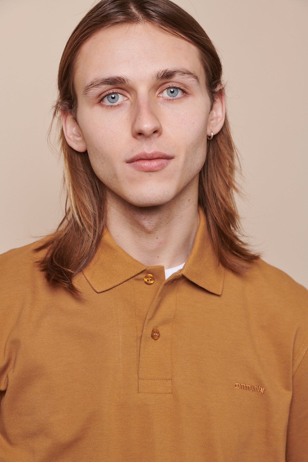 Portrait of male wearing short sleeve polo shirt in tan with top button undone showing crew neck white t shirt underneath