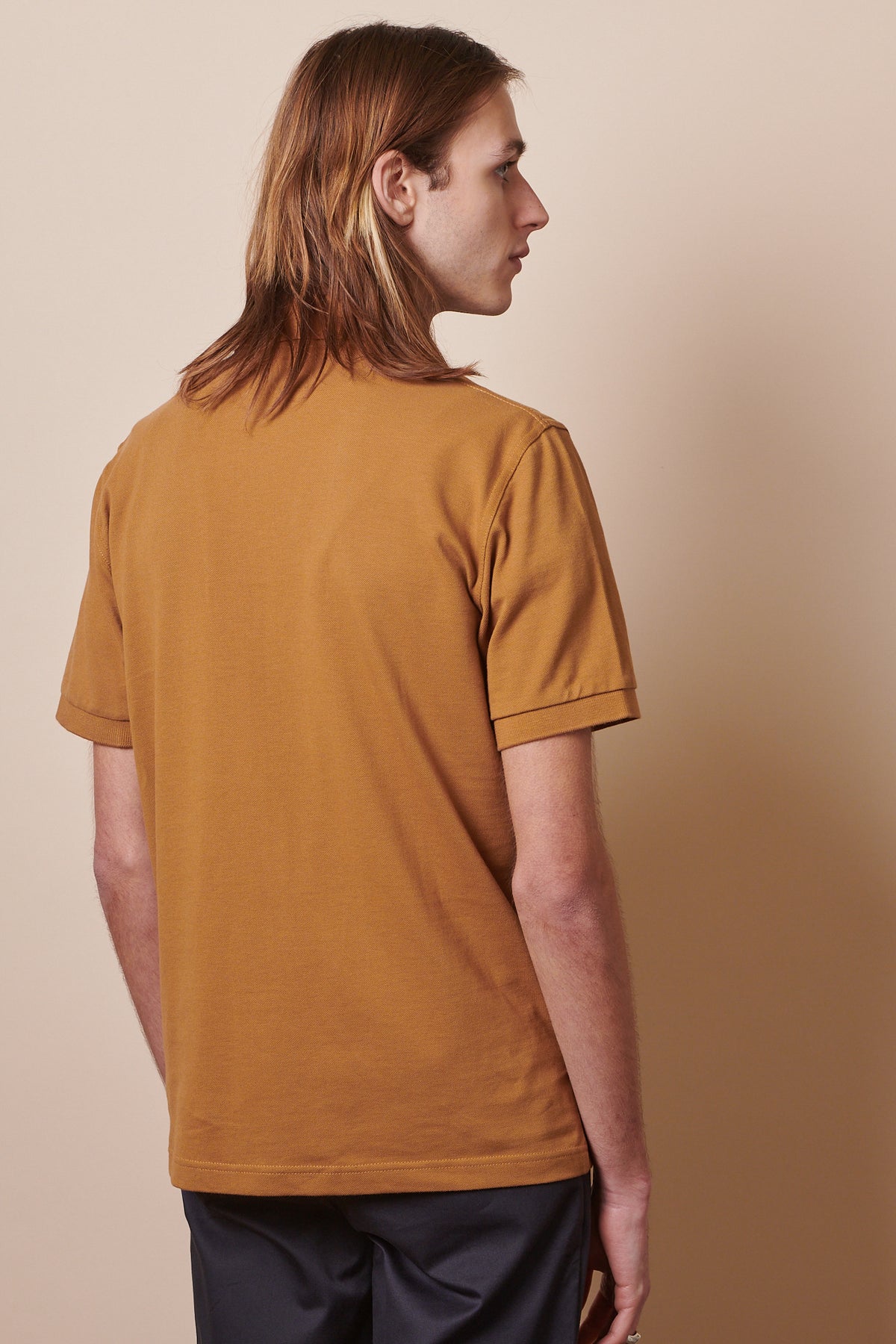 Thigh up image of the back of short sleeve polo shirt in tan