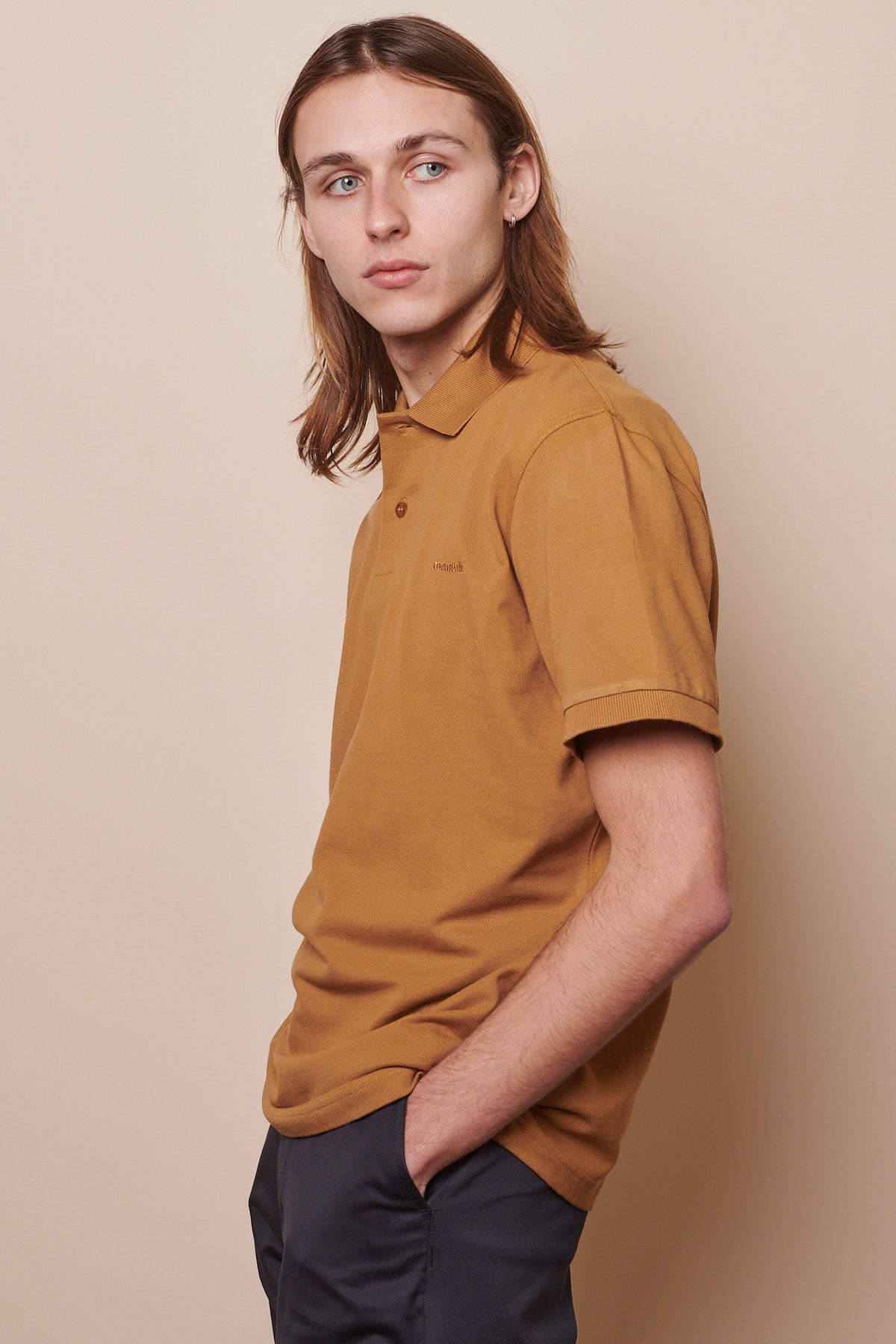 Thigh up image of the side of male wearing short sleeve polo shirt in tan with hands in pockets of chinos