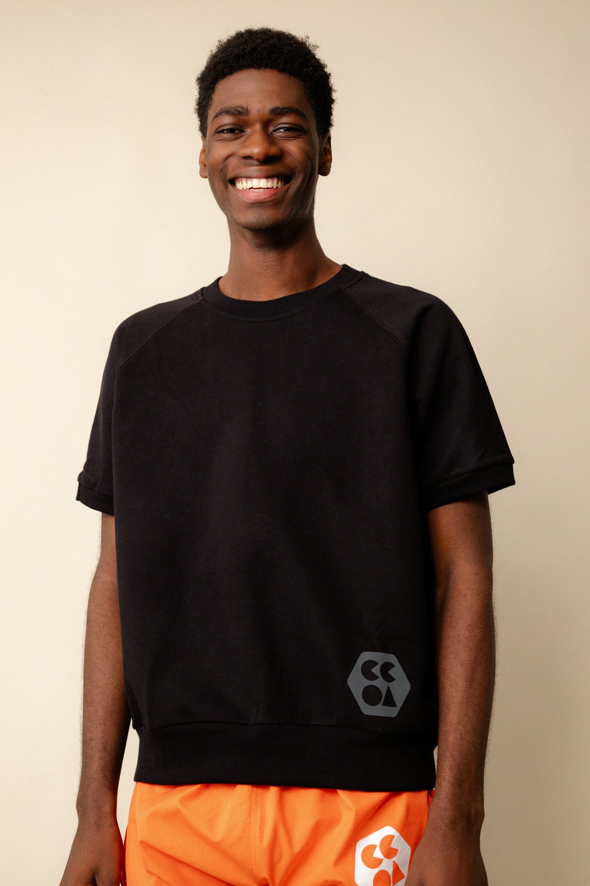 
            Smiley, black male wearing short sleeve raglan training top plastic free in black with CCOA logo