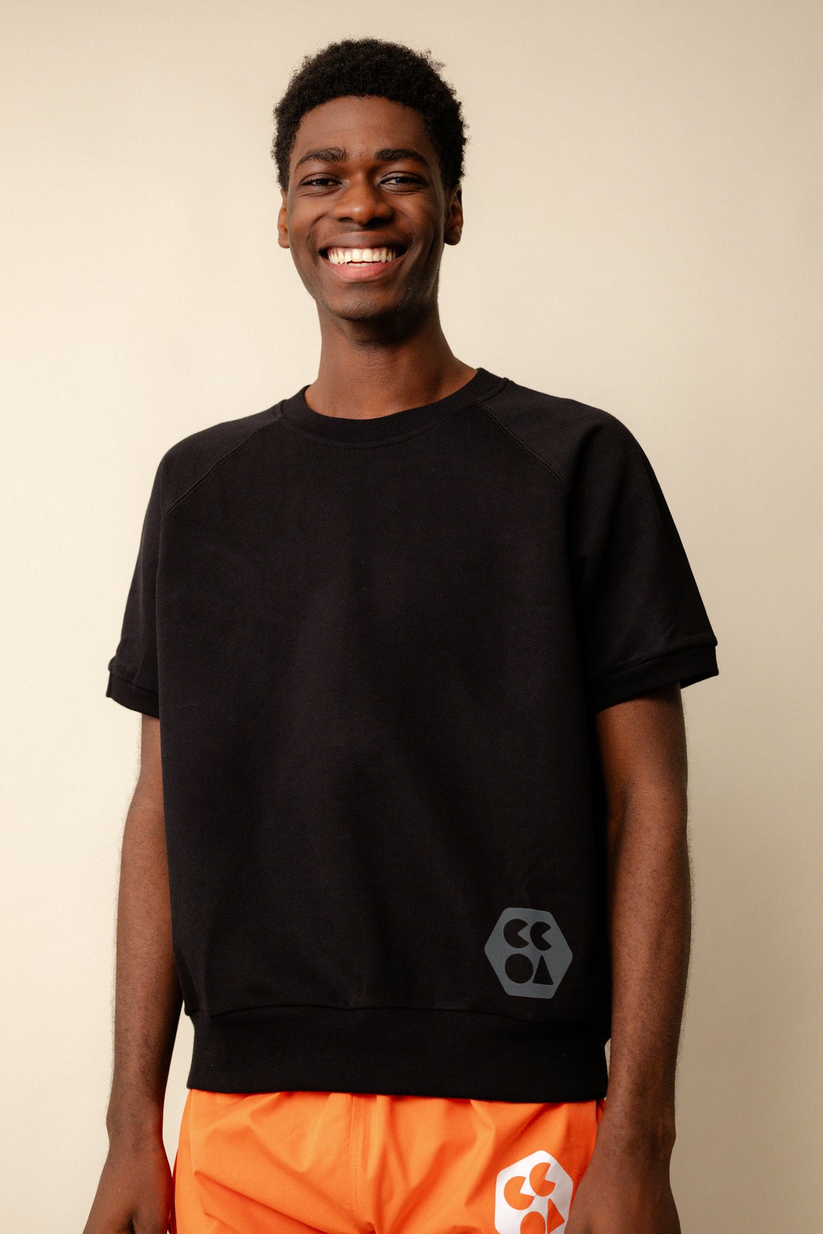 Smiley, black male wearing short sleeve raglan training top plastic free in black with CCOA logo