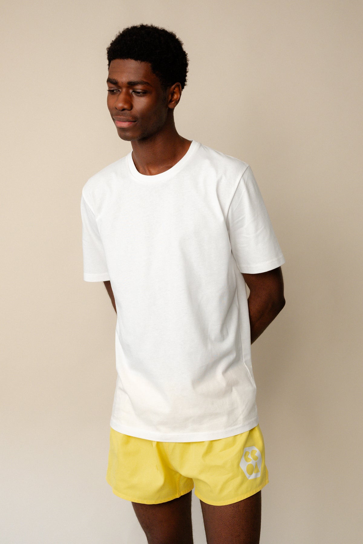 thigh up image of male wearing short sleeve t shirt plastic free in white paired with canary yellow lightweight sports short with CCOA logo