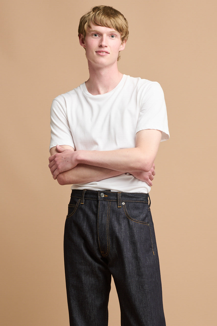 
            Thigh up front of male wearing short sleeve t shirt plastic free in white paired with arran jeans in indigo