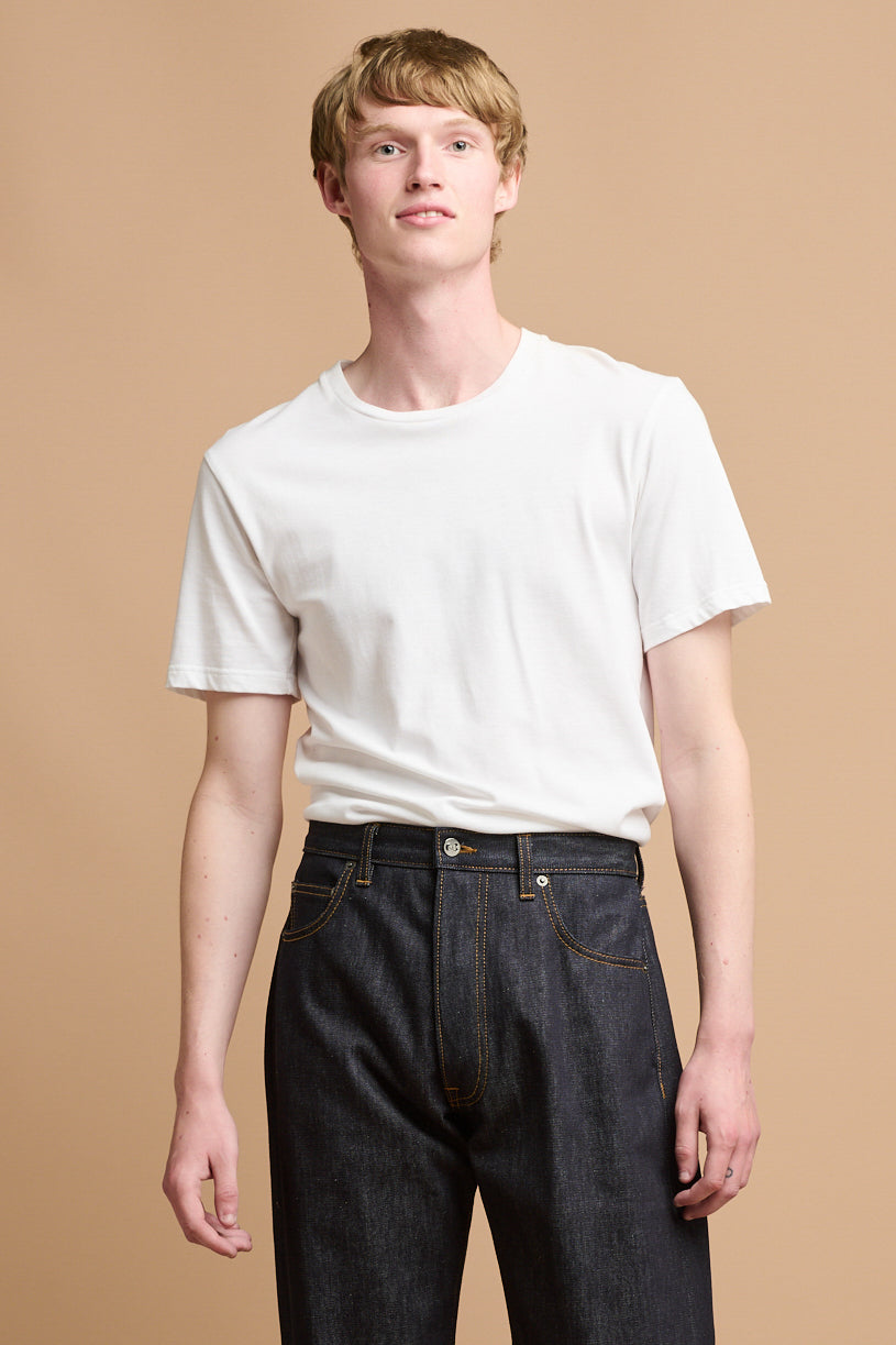 Thigh up of male wearing plastic free short sleeve t shirt in white paired with button fly Arran jean in indigo