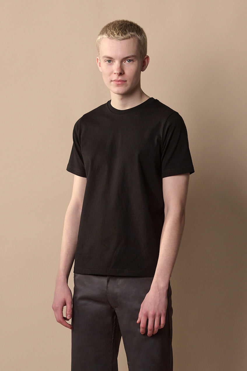 Thigh up front of male with short blond hair wearing short sleeve t-shirt in black.