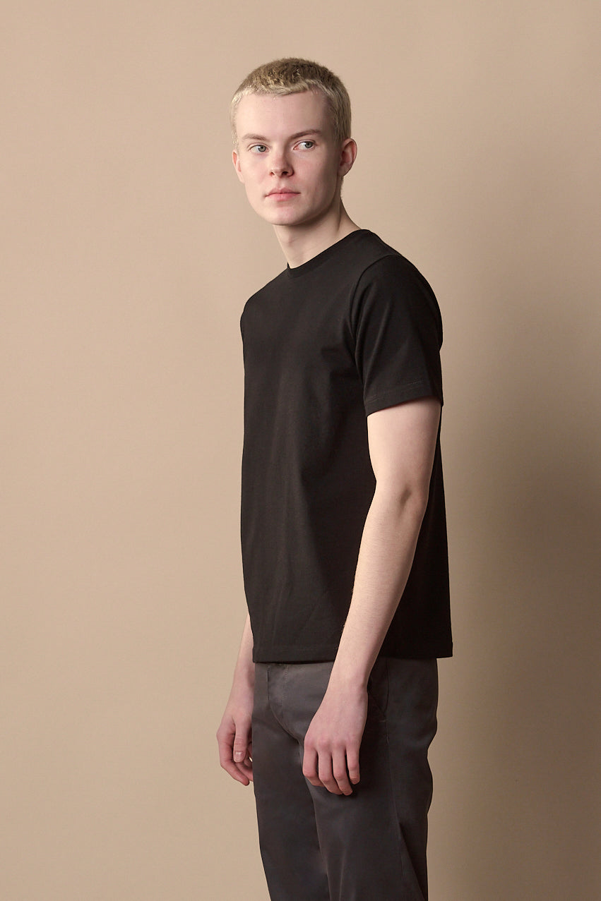 Thigh up side of male with short blond hair wearing short sleeve t-shirt in black.