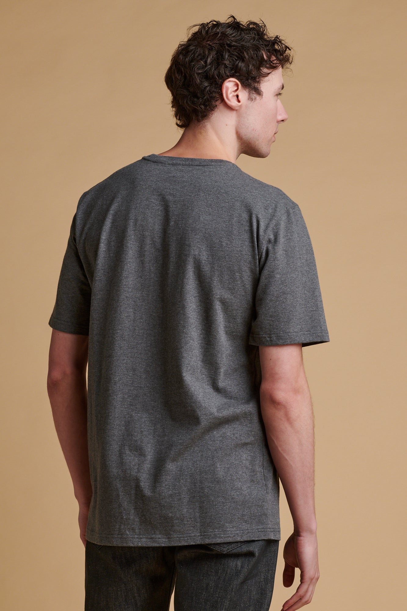 Thigh up of the back of male wearing short sleeve t shirt in charcoal.