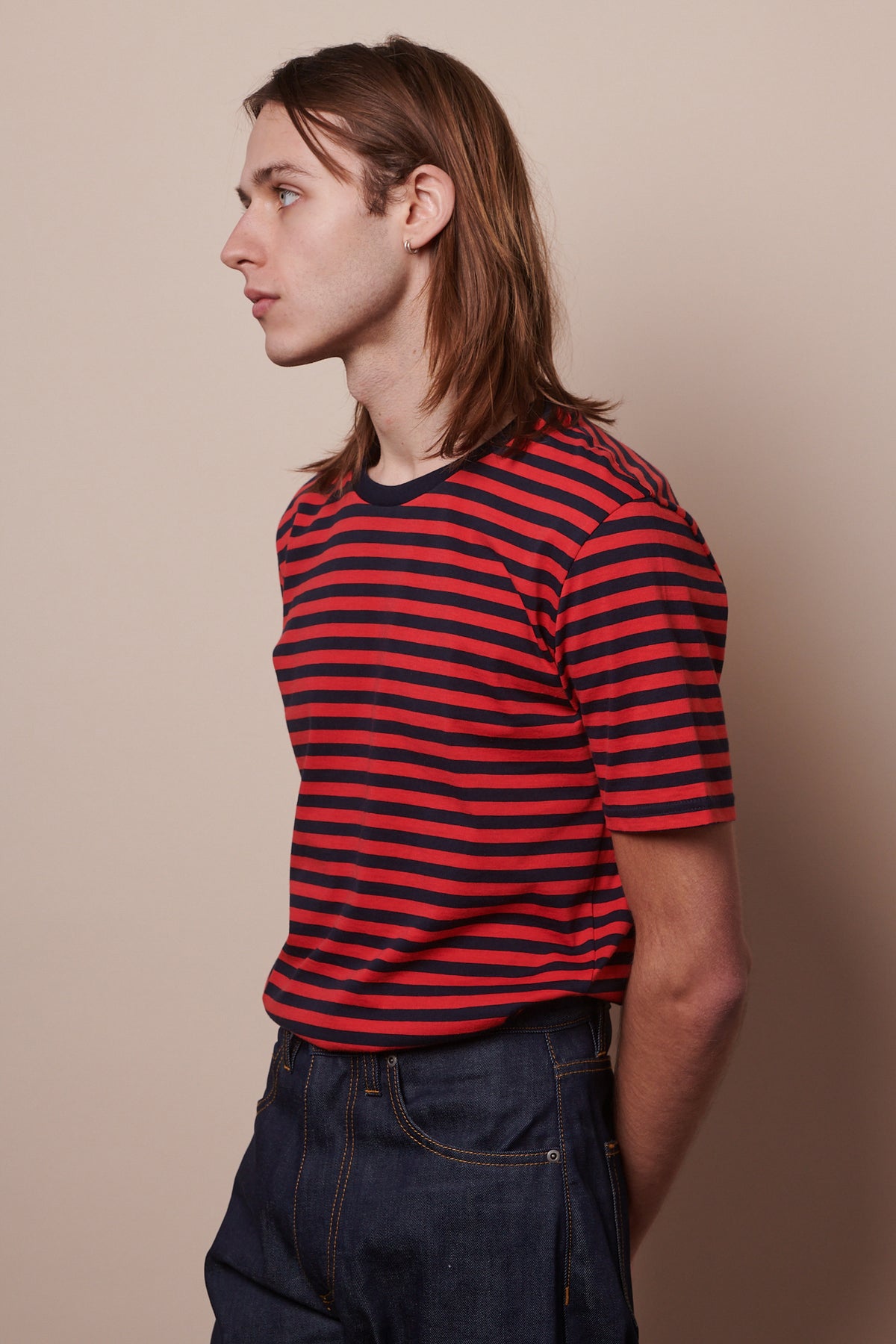 thigh up image of male from the side wearing short sleeve t shirt in navy red stripes tucked into indigo jeans