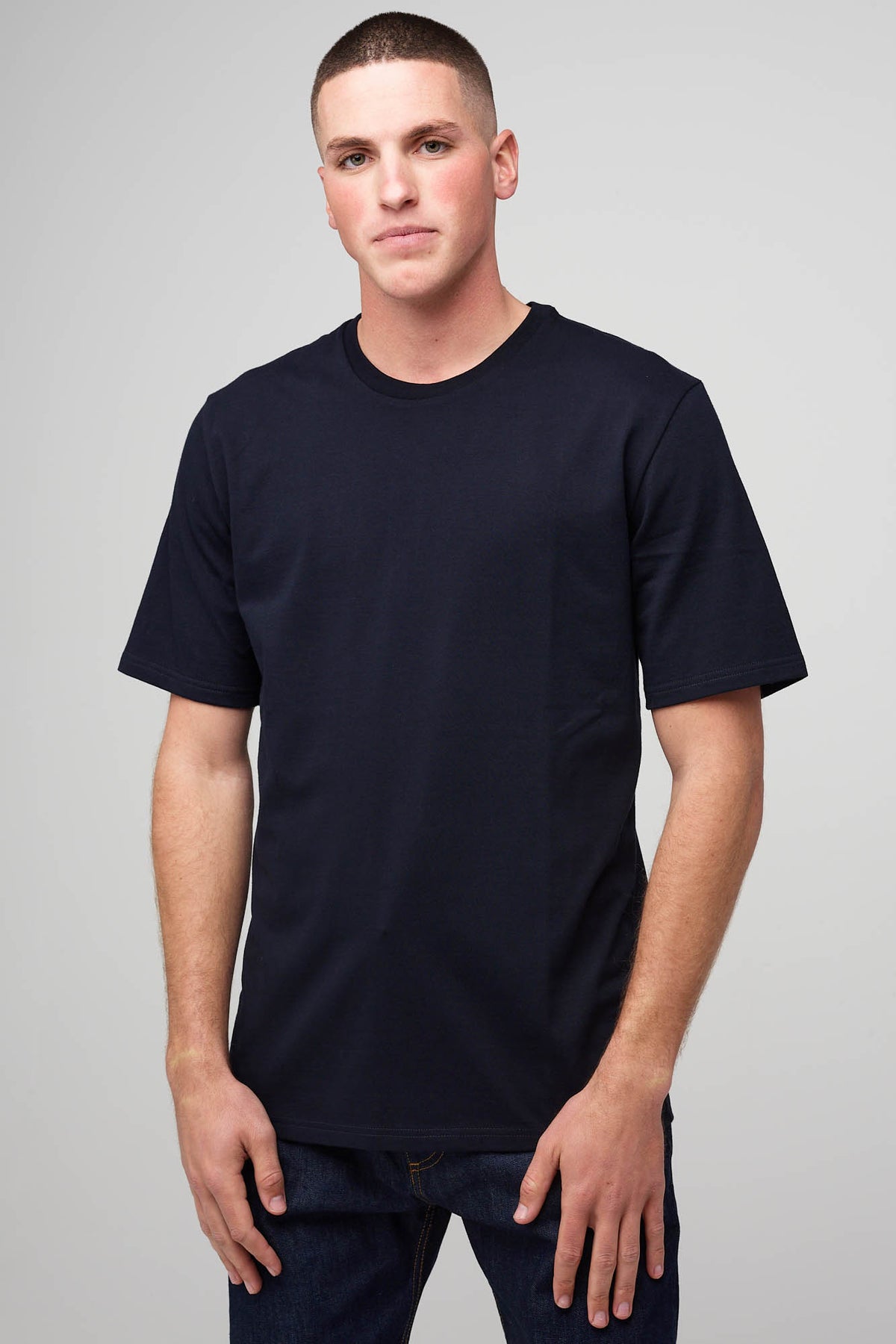 Thigh up image of male with a shaved head wearing short sleeve T-shirt navy