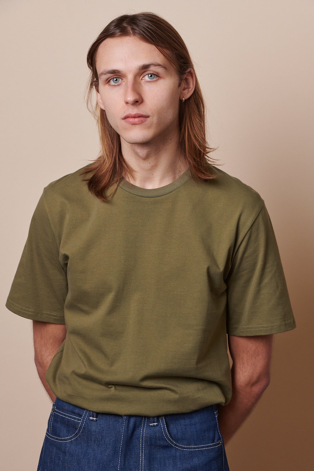 Male wearing short sleeve t shirt in olive tucked into jeans