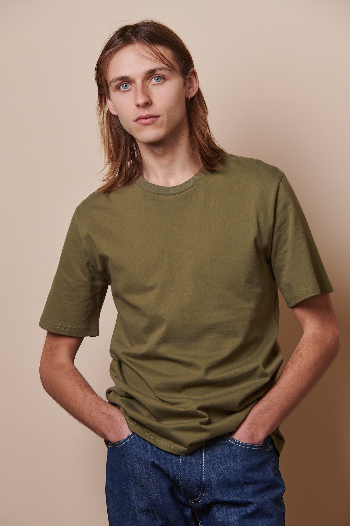 
            Thigh up male wearing short sleeve t shirt in olive with hands in pockets of jeans