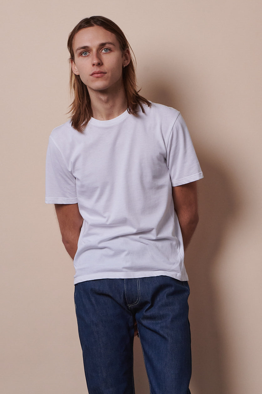 The front of male from the thigh up wearing short sleeve t shirt in white paired with blue jeans.