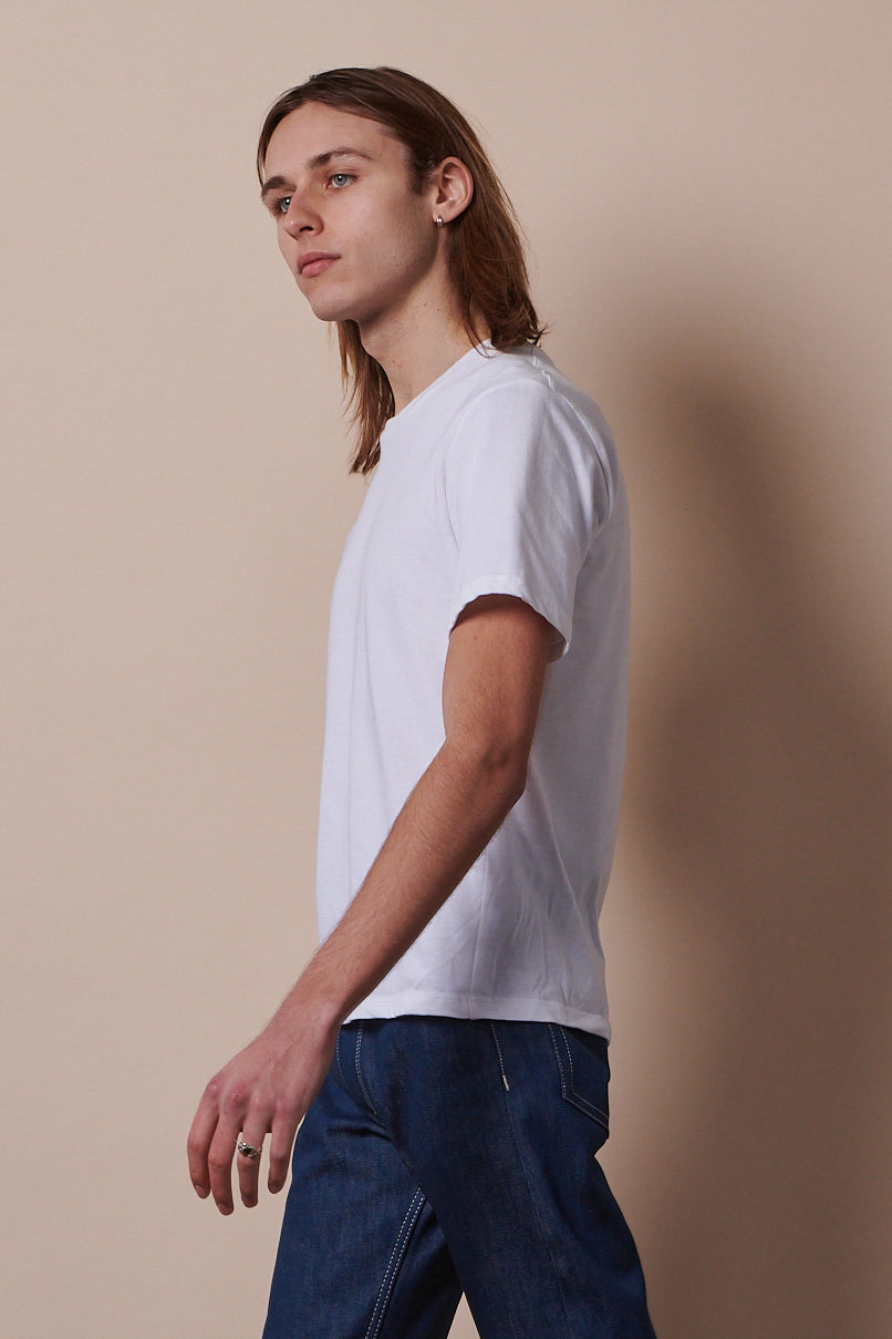 The side of male wearing short sleeve t shirt in white paired with blue jeans.