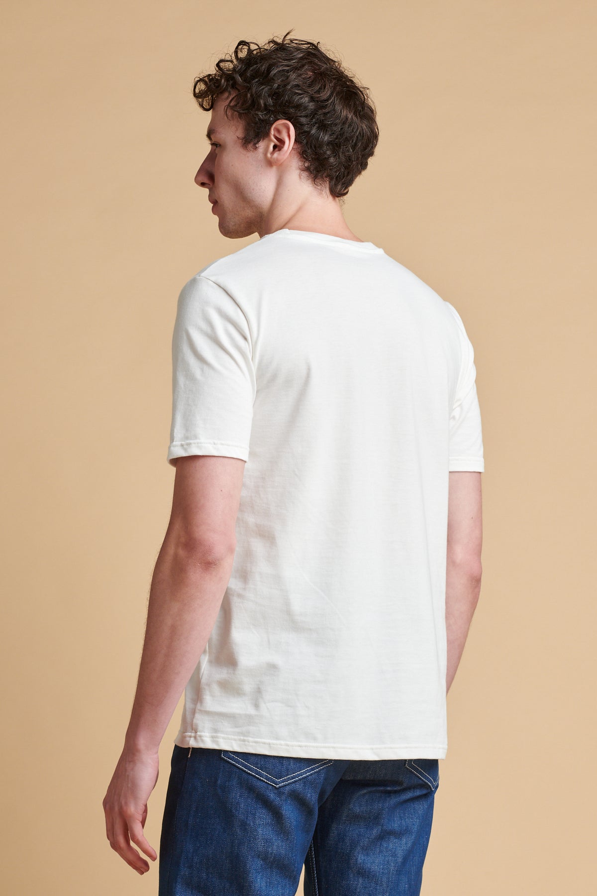 Man wearing a white t-shirt and blue jeans against a beige background