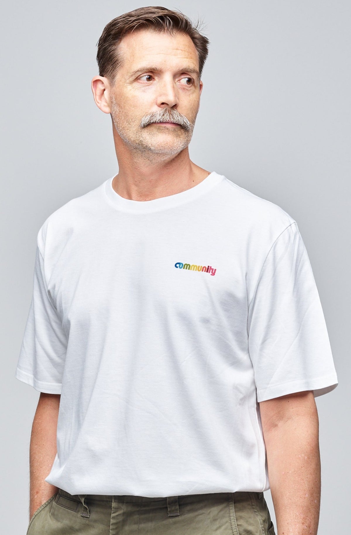 
            Community Clothing founder, Patrick Grant, wearing a white short sleeve t-shirt with branding on the chest. Styled tucked in