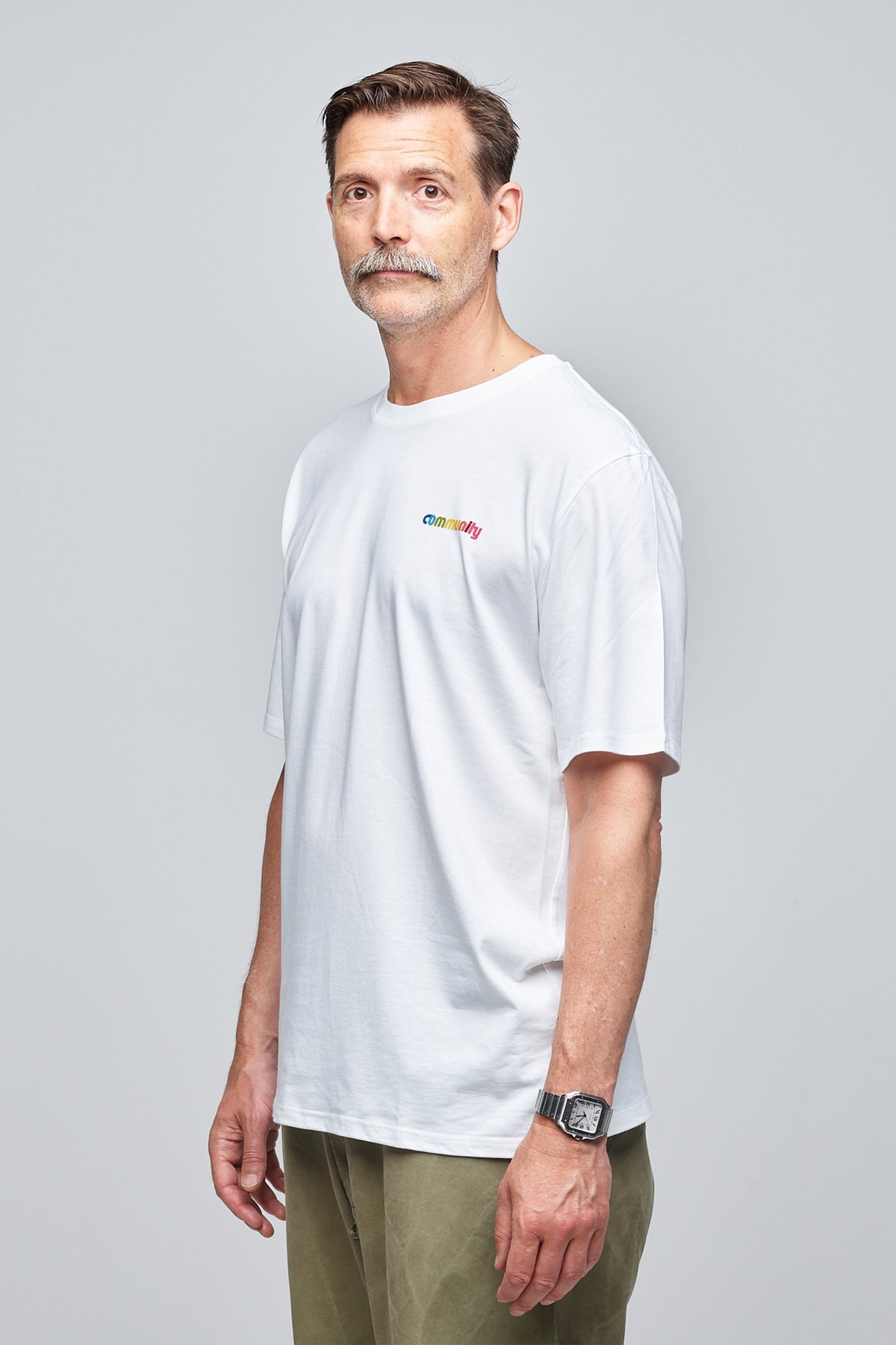 
            Community Clothing founder, Patrick Grant, wearing a white short sleeve t-shirt with branding on the chest. Styled untucked