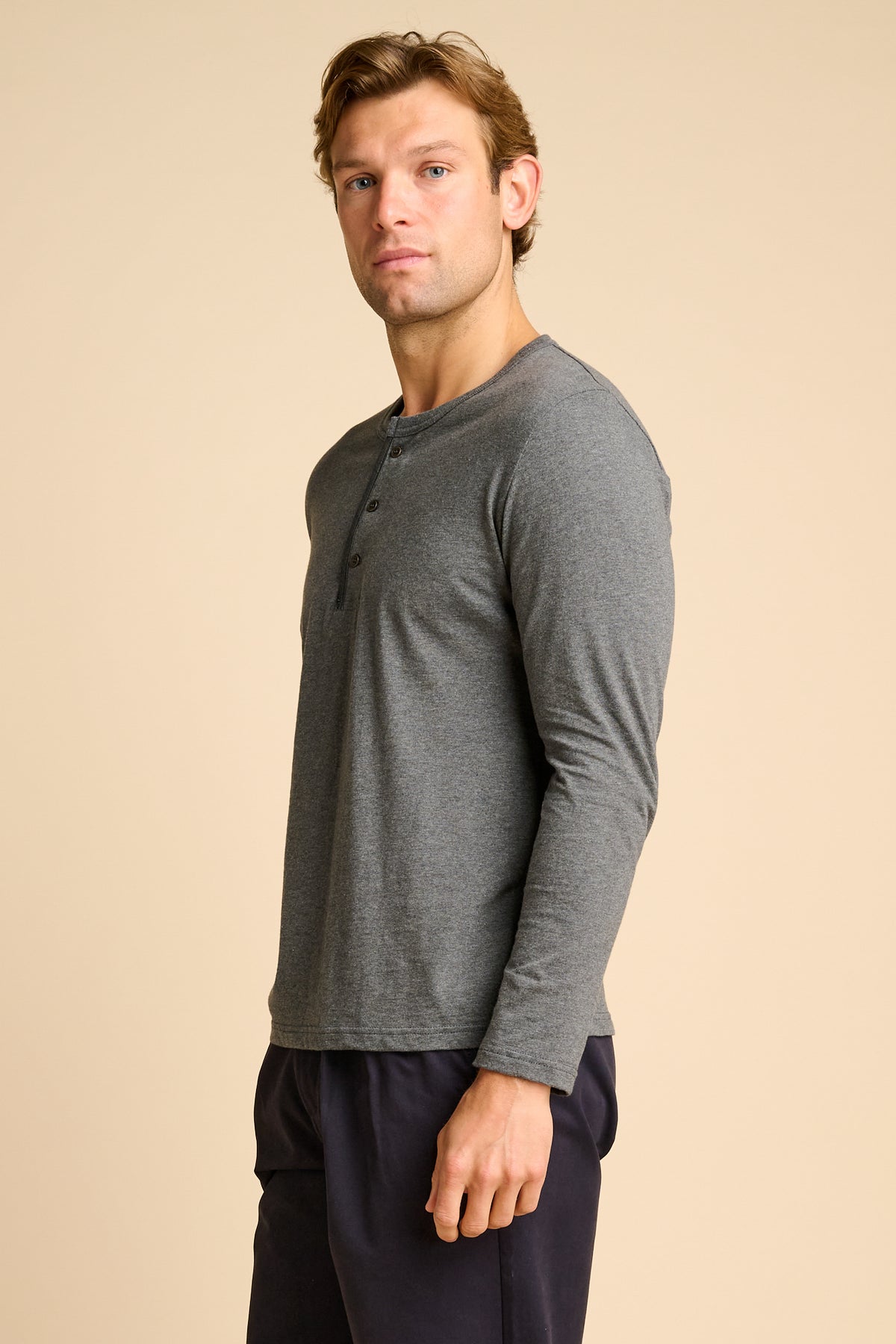 Man wearing a grey long-sleeve henley shirt and navy pants on a beige background.