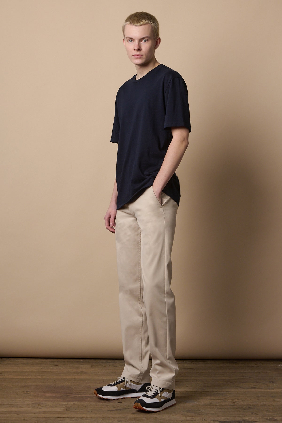 Full body image of white male wearing slim stretch chino in light stone paired with short sleeve crew neck t shirt in navy