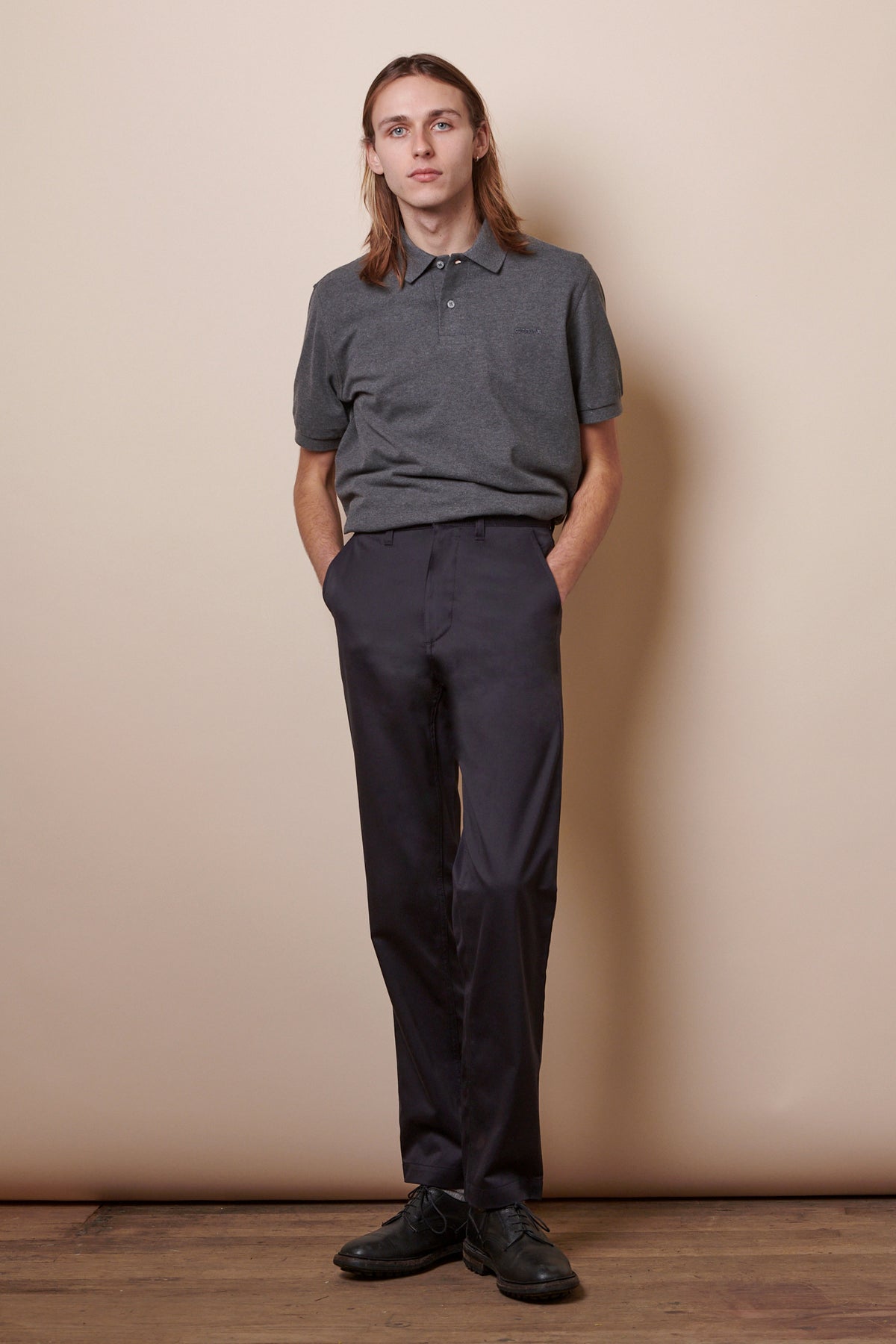 Full body image of white male with shoulder length brown hair wearing Men's Slim Stretch Chino in navy paired with short sleeve polo shirt