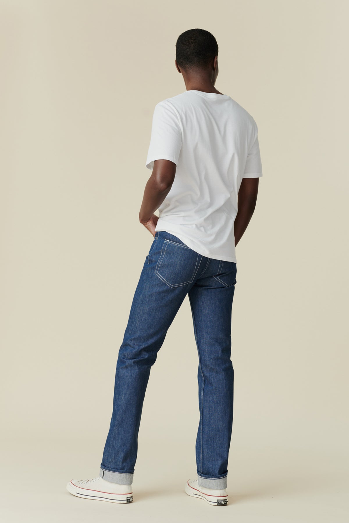 Person wearing a white t-shirt and blue jeans on a beige background