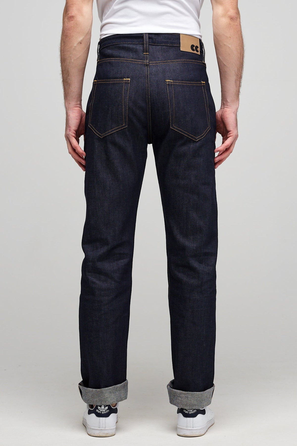 
            Waist down image of male wearing men&#39;s straight cut selvedge jeans in raw denim with two back pockets and CC logo jeans patch