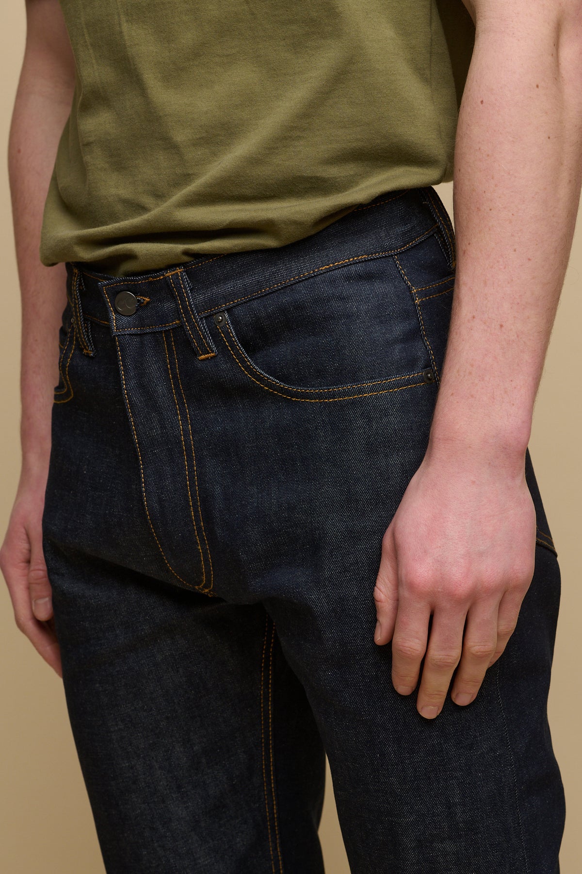 
            Close up detail shot of the back of men&#39;s straight cut selvedge jeans in indigo raw denim with tobacco contrast stitching.  Belt loops and CC logo jeans patch on the back of waistband with two back pockets.