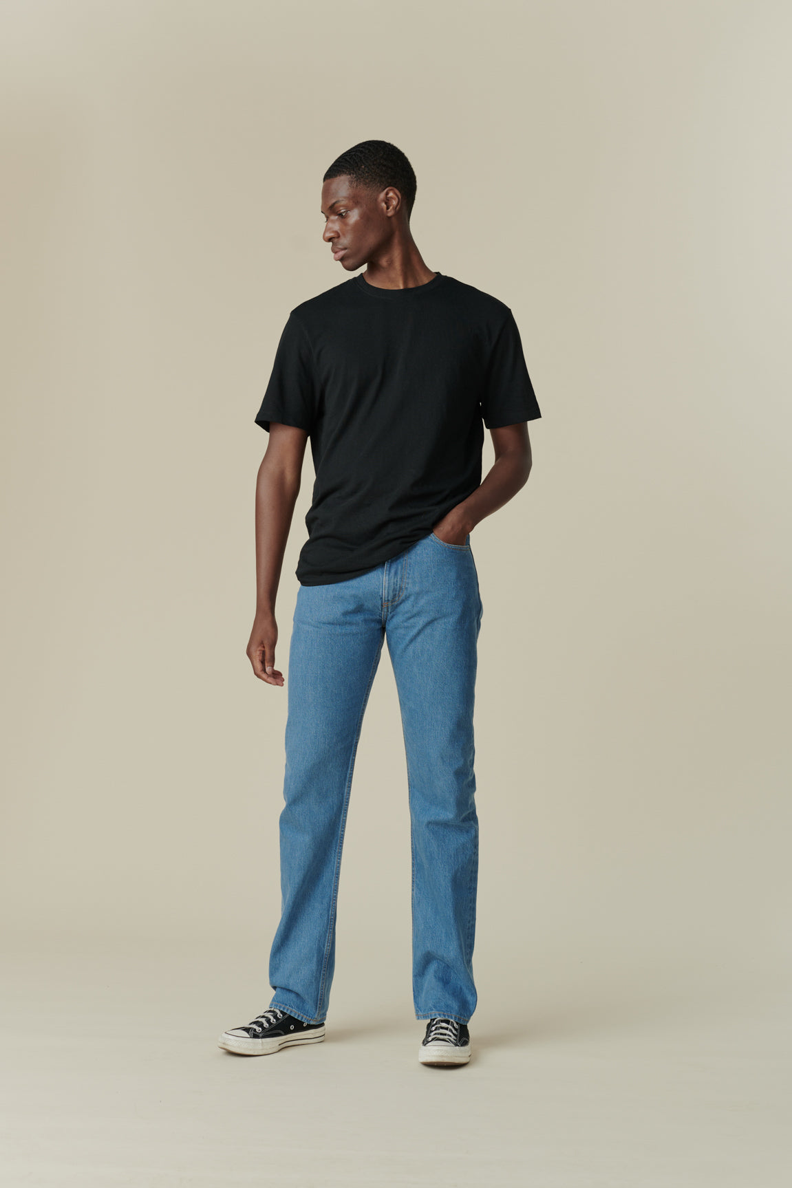 Full body shot of front of black male with short dark hair wearing men's straight cut selvedge jeans in fade with a black short sleeve t-shirt.
