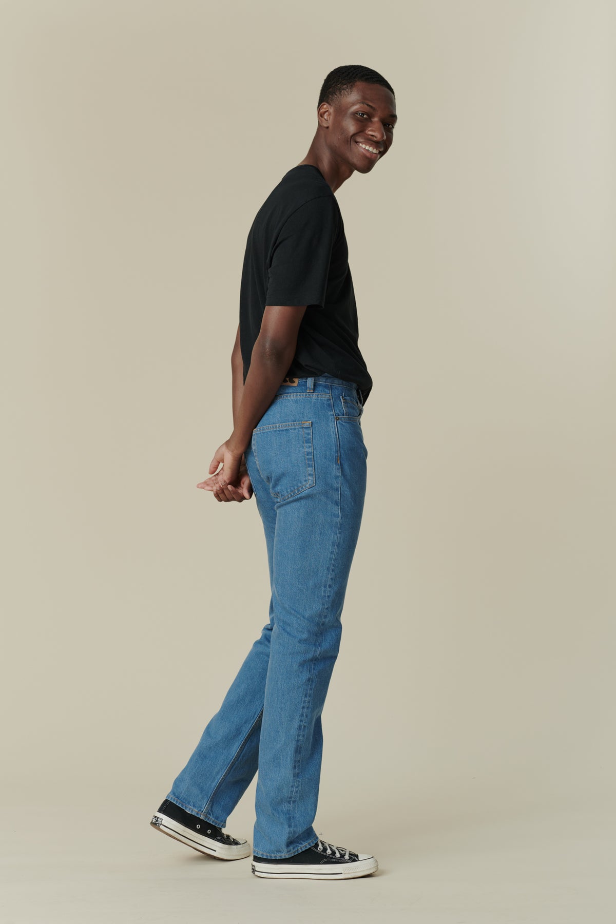 Side angle shot of front of black male with short dark hair wearing men's straight cut selvedge jeans in fade with a black short sleeve t-shirt.