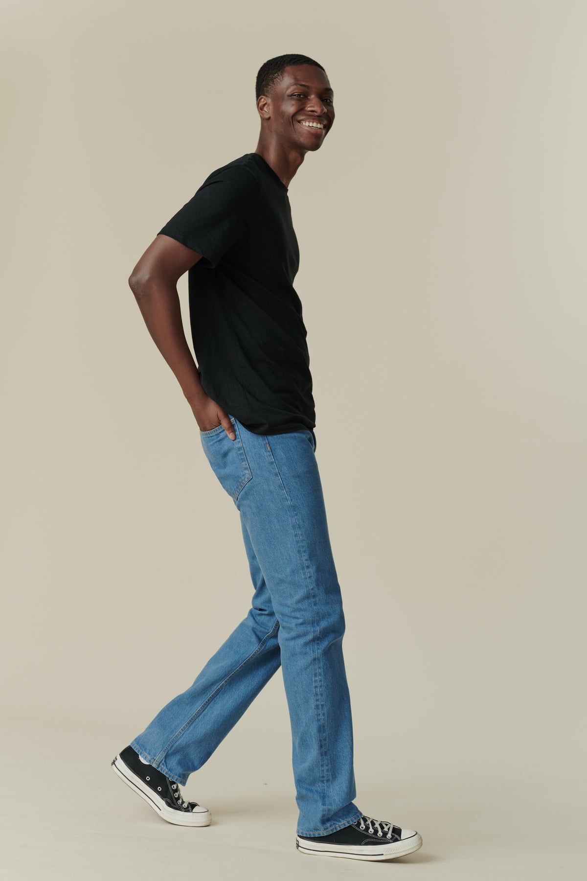 Full body side shot of black male with short dark hair, wearing men's straight cut selvedge jeans in fade with a black short sleeve t-shirt.
