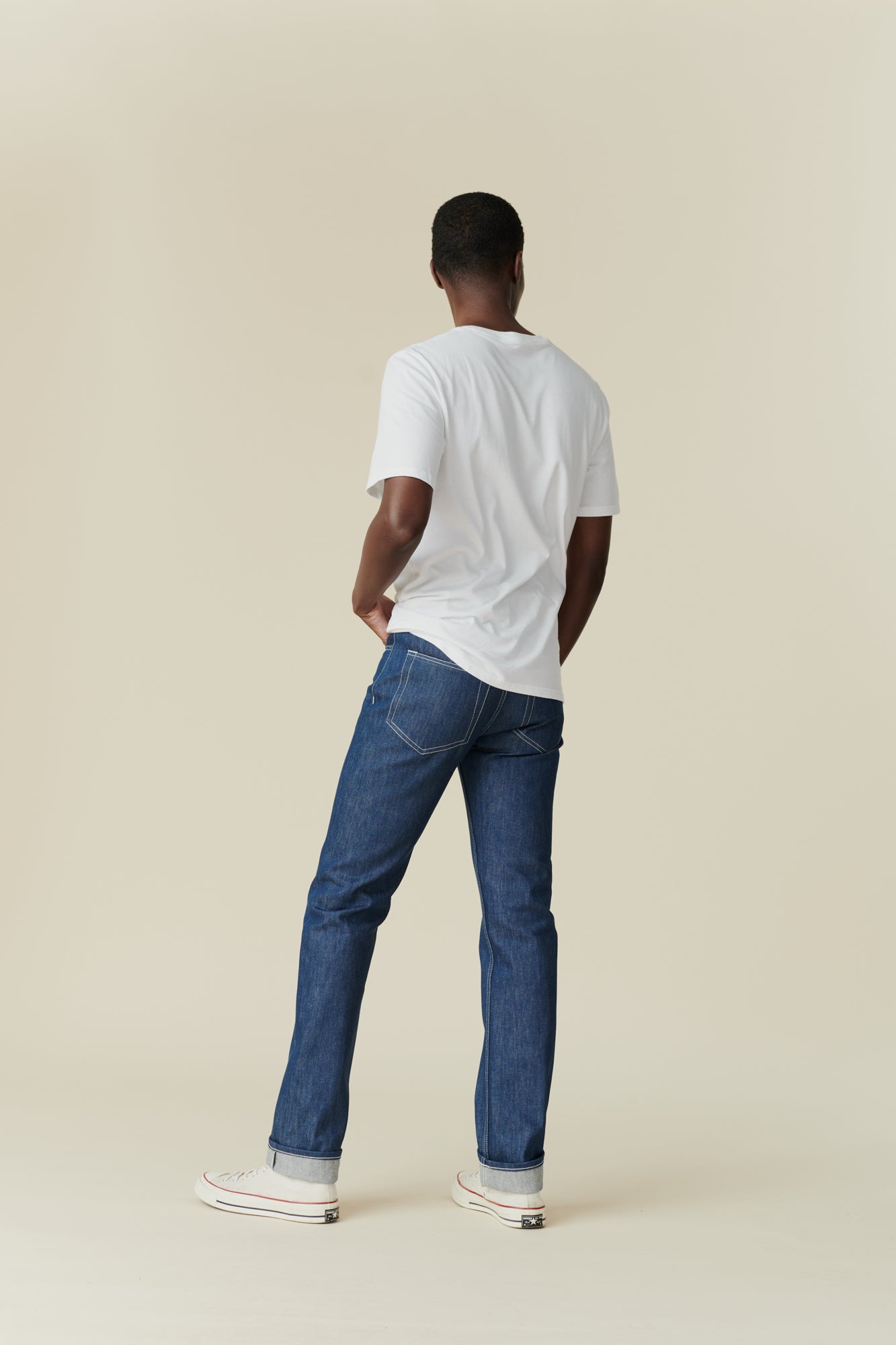 Full body back image of black male wearing straight cut jeans in blue, rolled hem. 