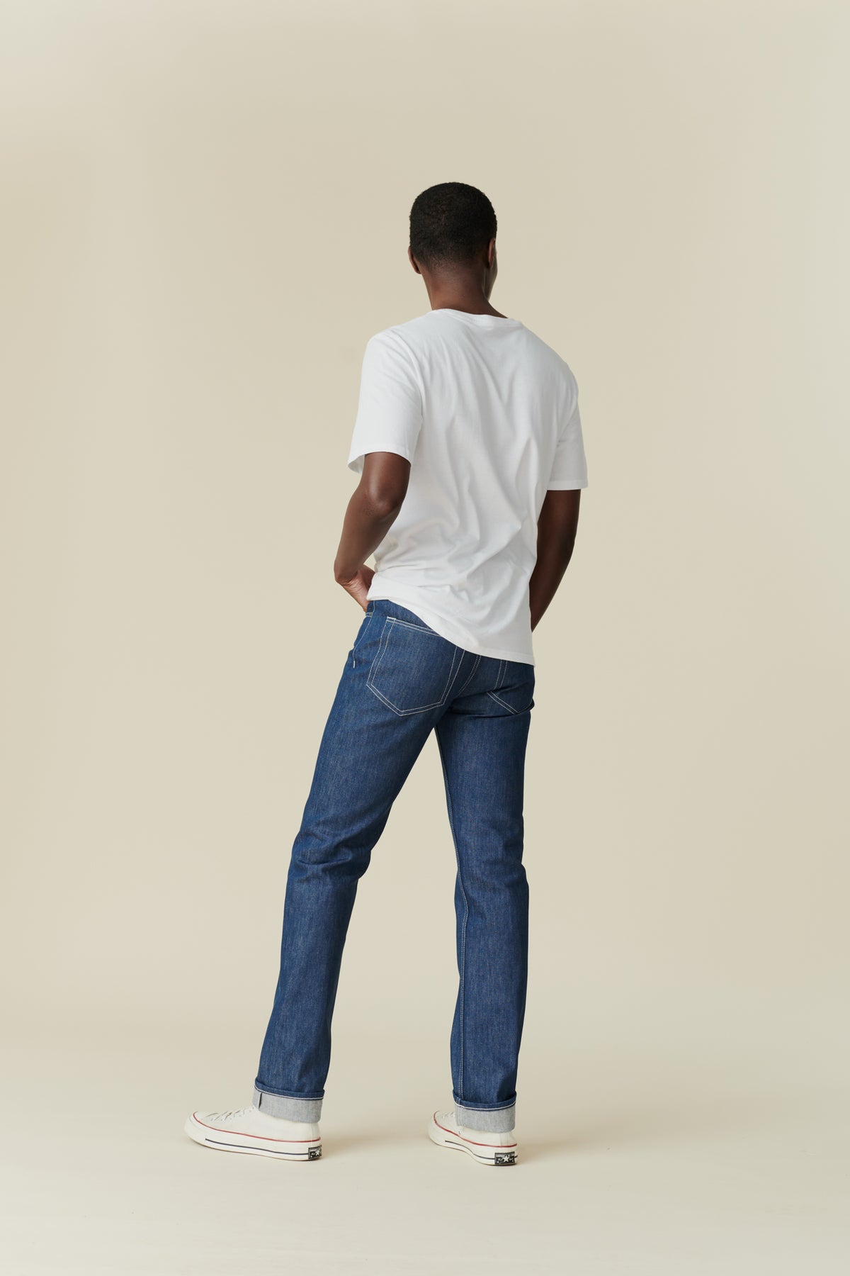 Full body back image of black male wearing straight cut jeans in blue, rolled hem.