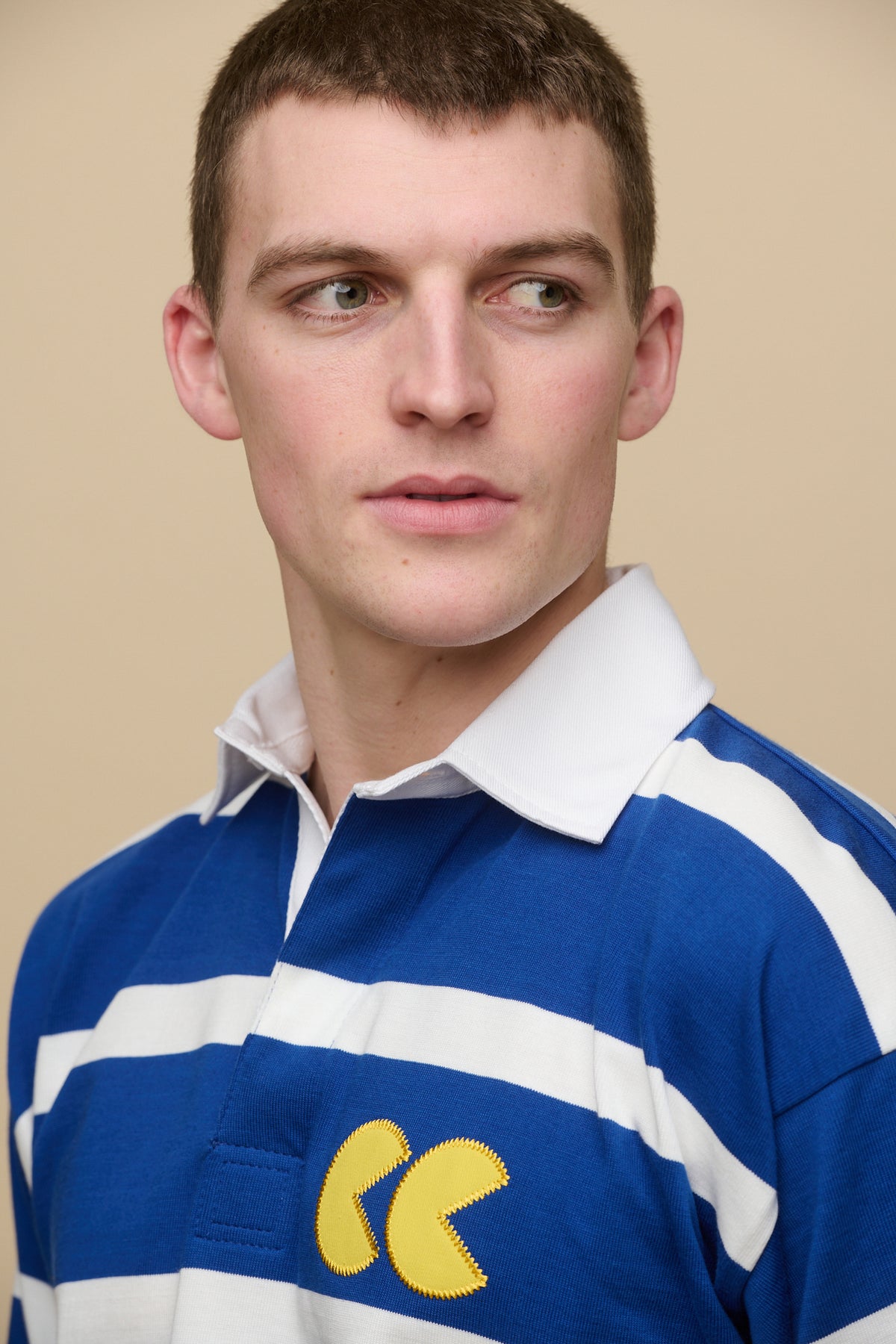 
            Close up portrait of male with shaved brown hair wearing stripe logo rugby shirt in blue white stripe with yellow CC logo aplique patch on chest