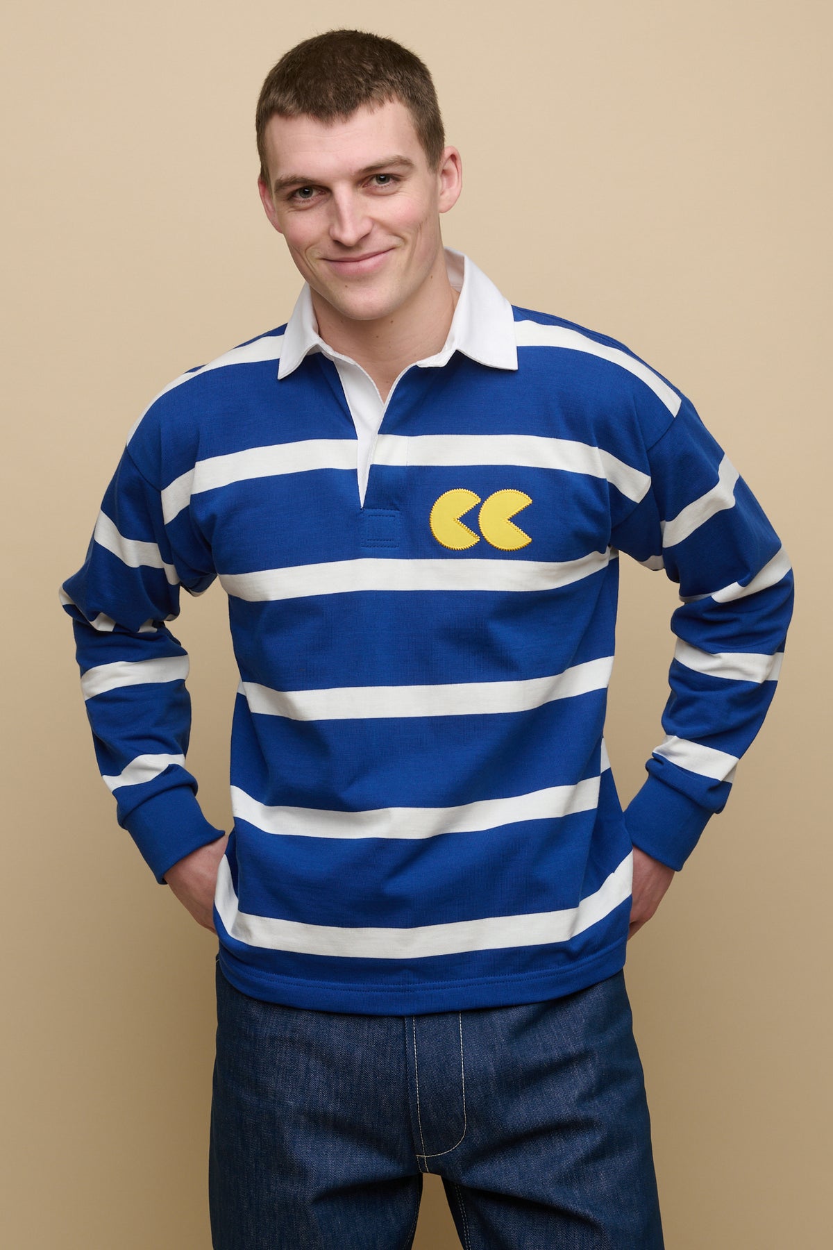 
            Smiley, brunet male with shaved brown hair wearing stripe logo rugby shirt in blue white stripe with yellow CC logo applique patch on chest