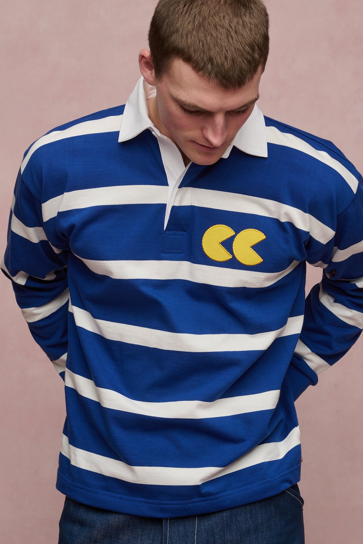 
            Thigh up image of male with shaved brown hair wearing stripe logo rugby shirt in blue white stripe with yellow CC logo applique patch on chest