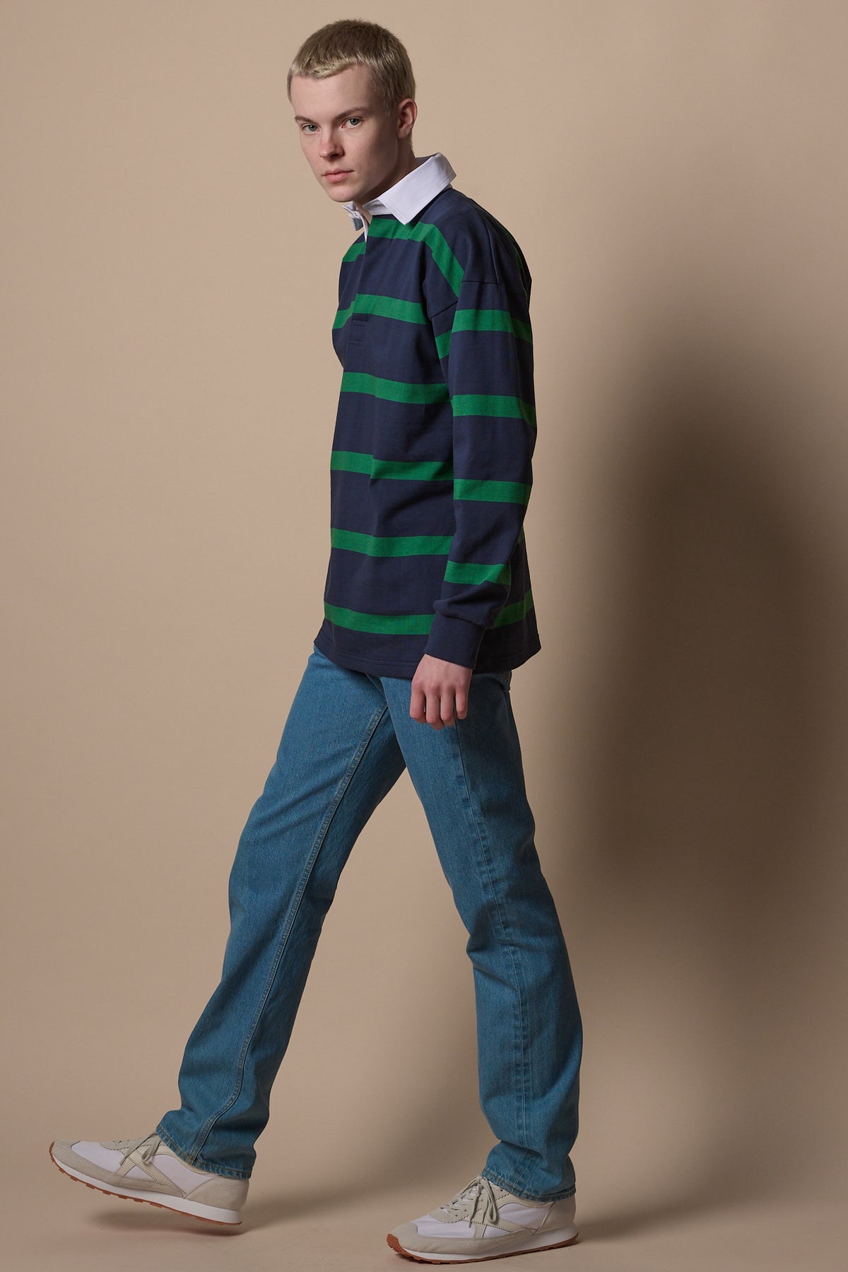 
            blonde male wearing stripe rugby shirt in navy emerald worn with blue jeans. 