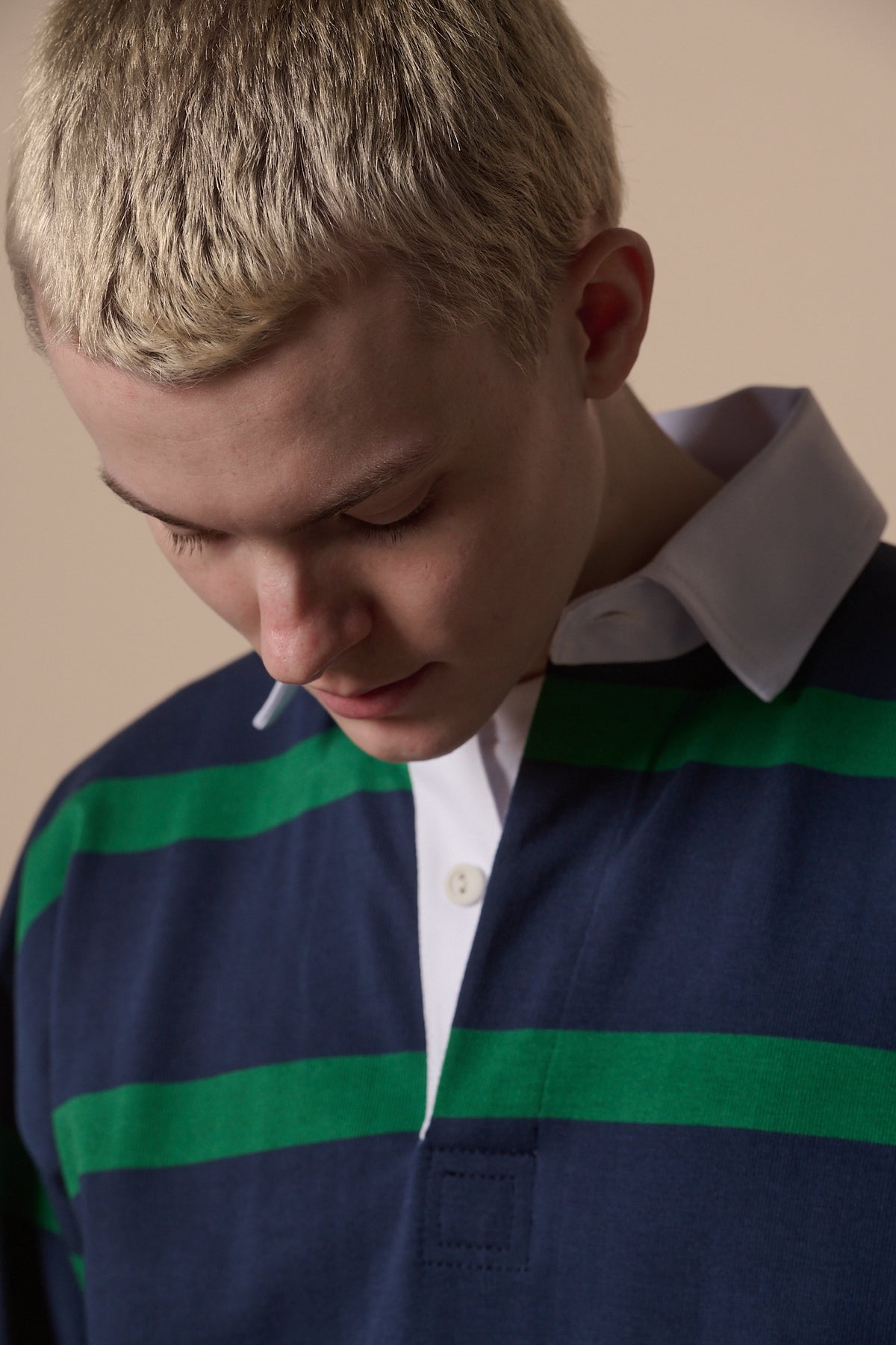 
            portrait of blonde male looking down wearing navy emerald rugby shirt with white collar.