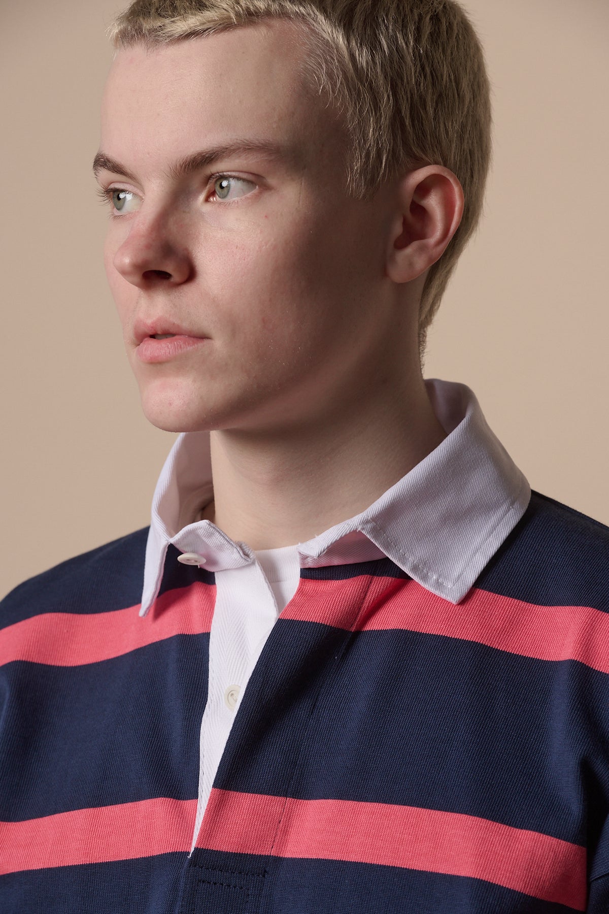 
            Portrait of blonde male wearing rugby shirt in navy pink with white collar unbuttoned over white t shirt